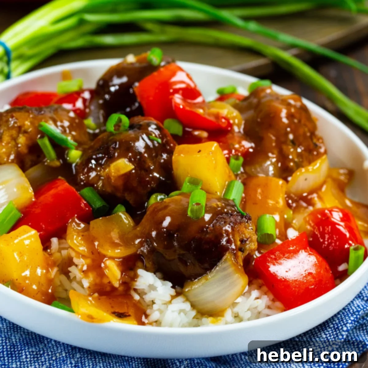 Plate of Sweet and Sour Meatballs served over white rice, garnished with fresh green onions.