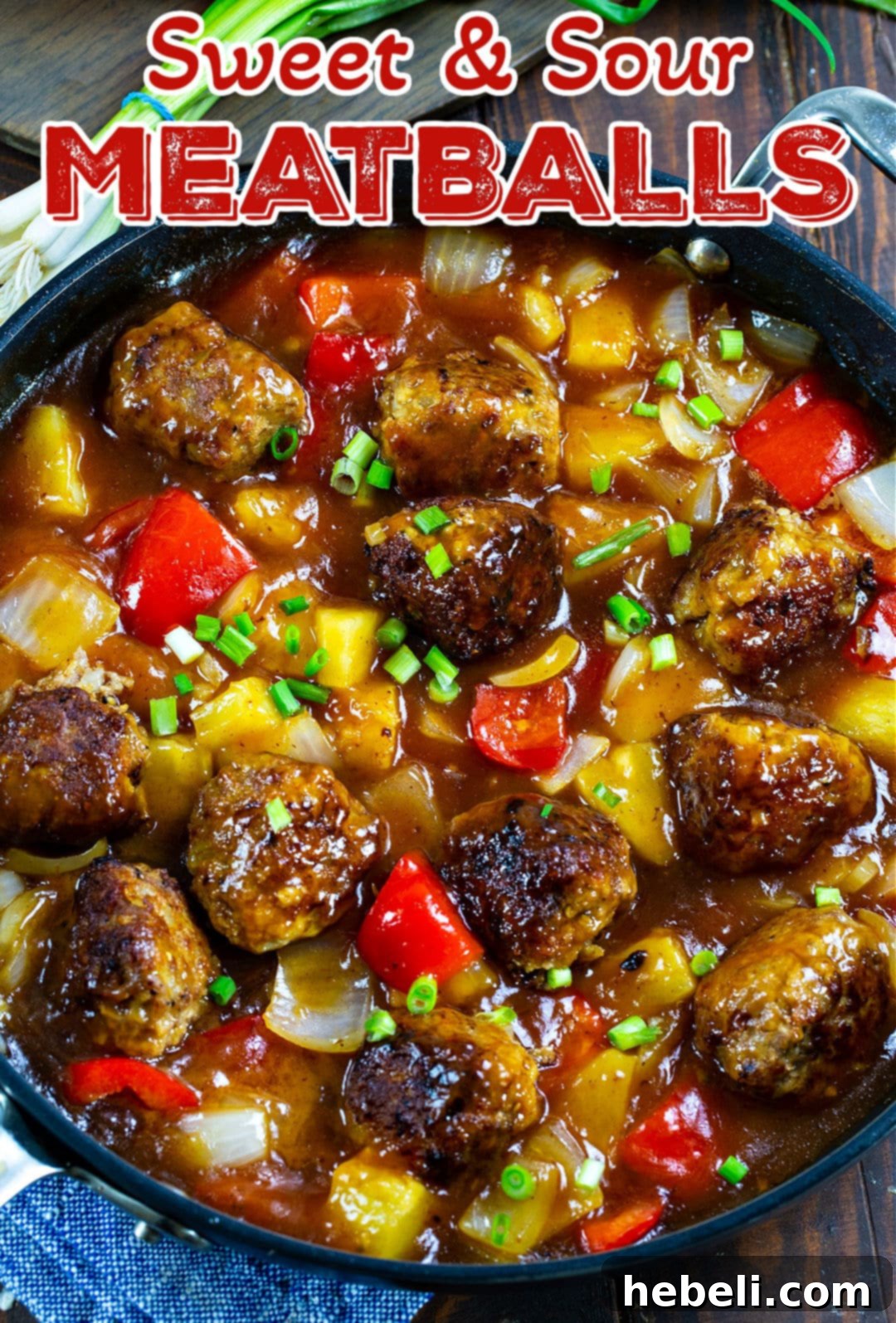 Sweet and Sour Meatballs simmering in a large nonstick skillet with pineapple chunks and colorful bell peppers.