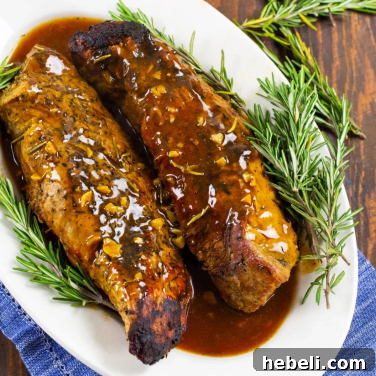 Two pieces of Slow Cooker Honey Garlic Pork Tenderloin on a platter with fresh rosemary, ready to serve.