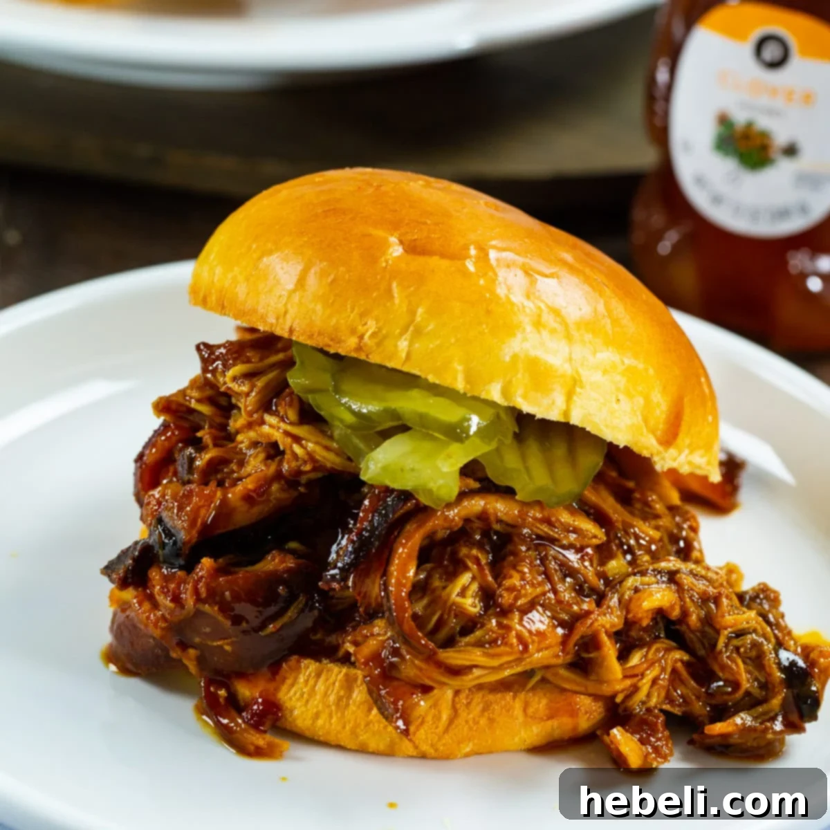 Slow Cooker Hot Honey Chicken on a bun with pickles, highlighting its delicious texture and vibrant sauce.