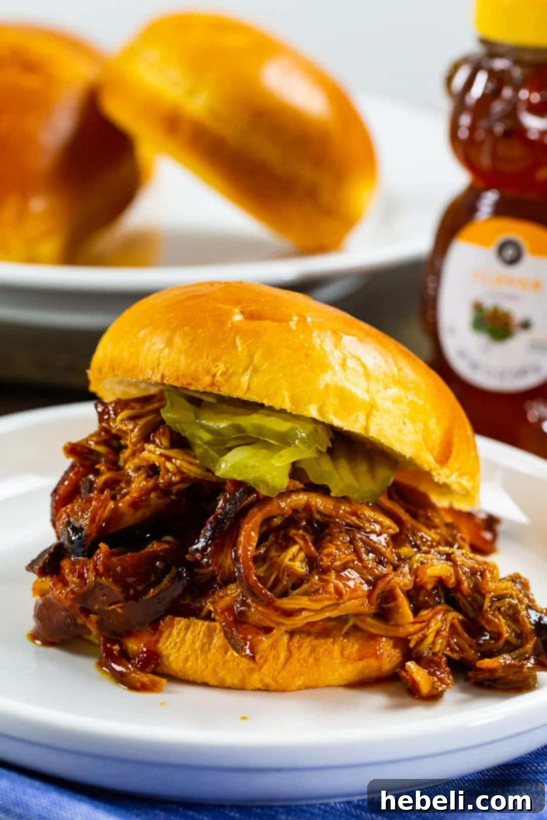 A close-up of Slow Cooker Hot Honey Chicken served on a bun, showcasing its rich texture and glossy sauce.