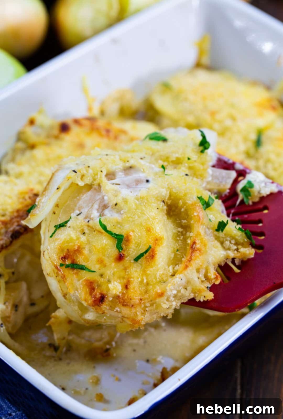 Sweet & Creamy Vidalia Gratin 6 A spatula lifting a portion of Baked Vidalias Au Gratin out of the baking dish, showing its creamy layers.