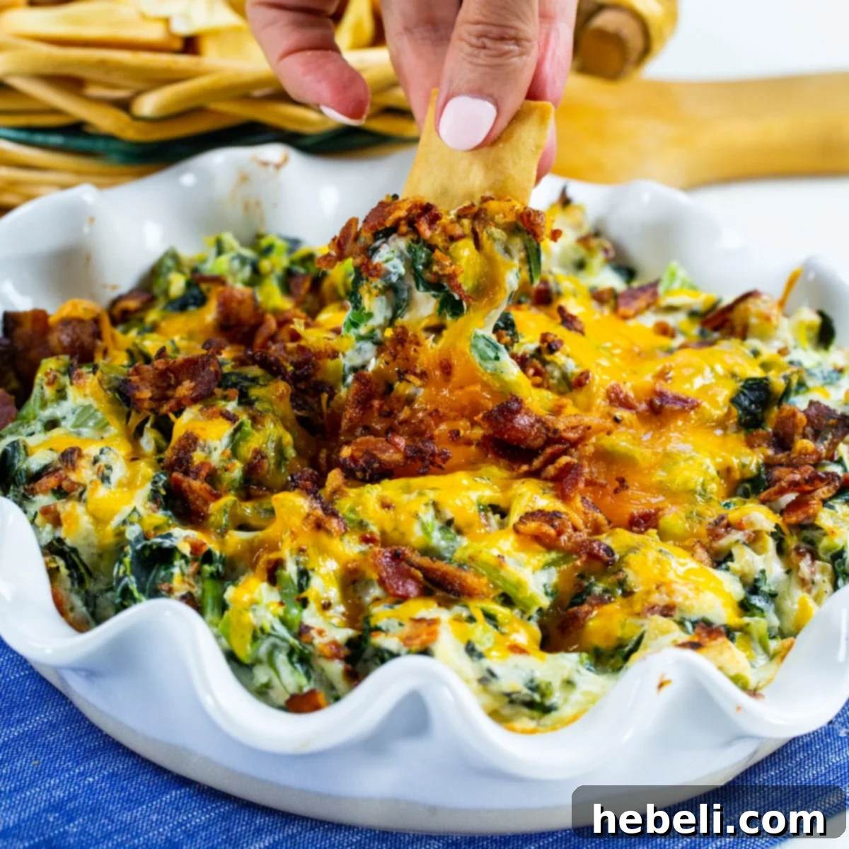 A golden-brown pita chip perfectly scooping up a generous portion of warm, bubbly Collards Artichoke Dip, highlighting its creamy texture and visible collard greens.