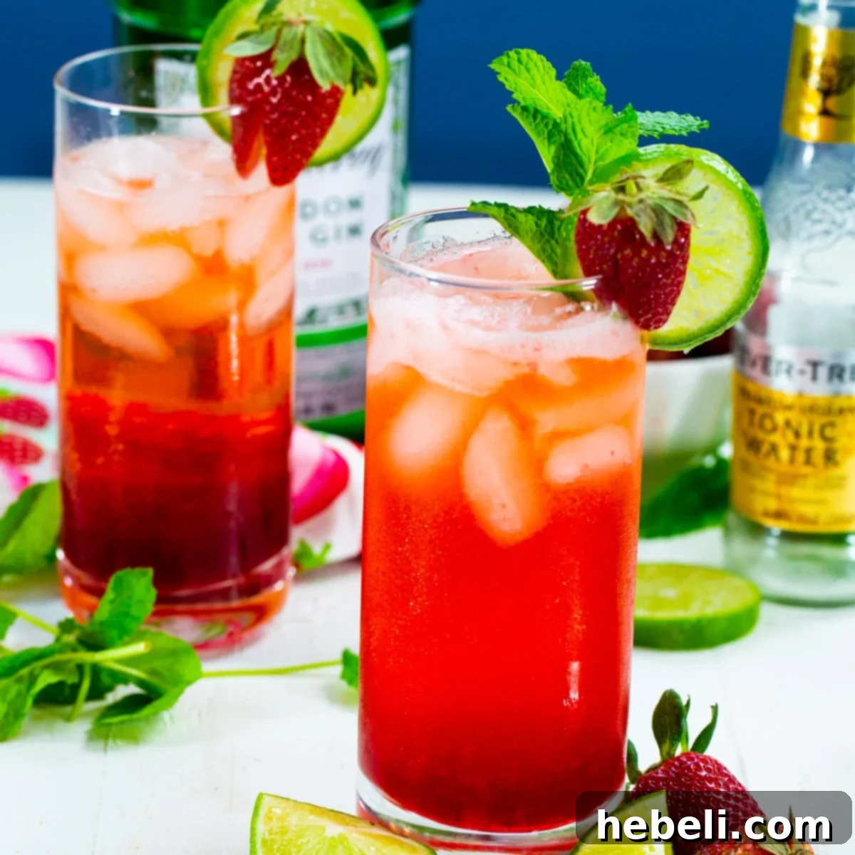 Two glasses of vibrant red Strawberry Gin and Tonic garnished with fresh strawberries and lime.