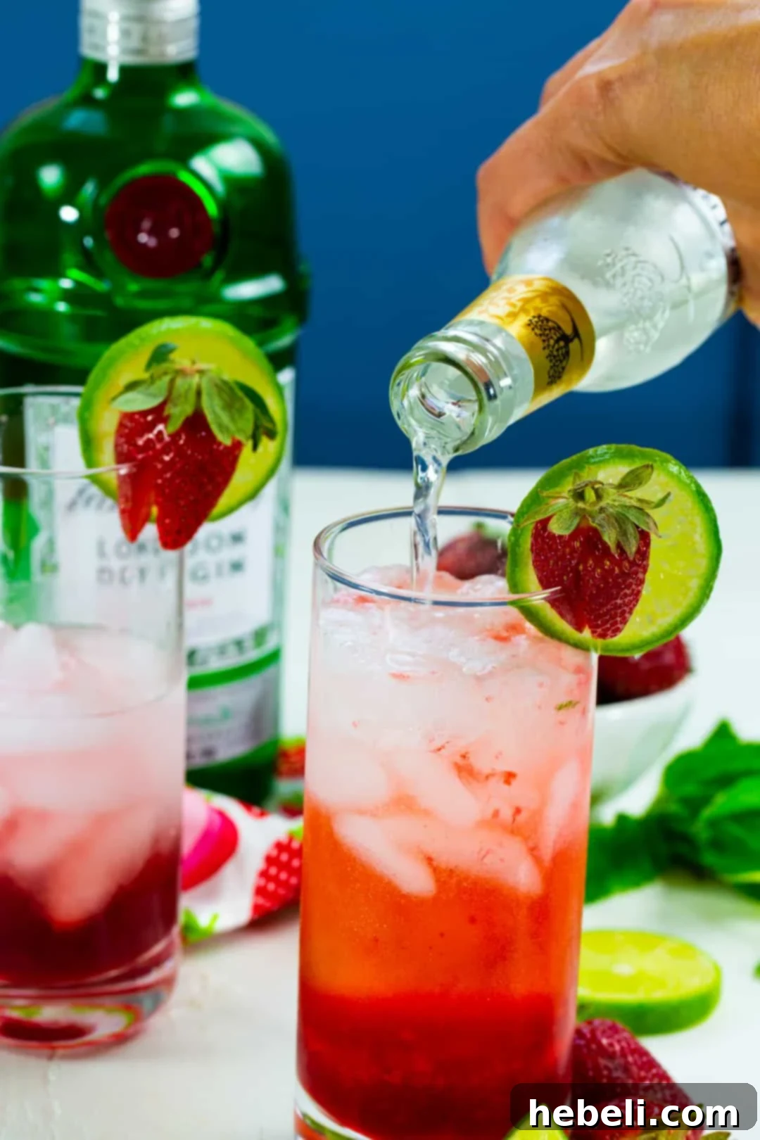 A bartender pouring tonic water into a glass filled with strawberry syrup and gin, creating a beautiful layered effect.