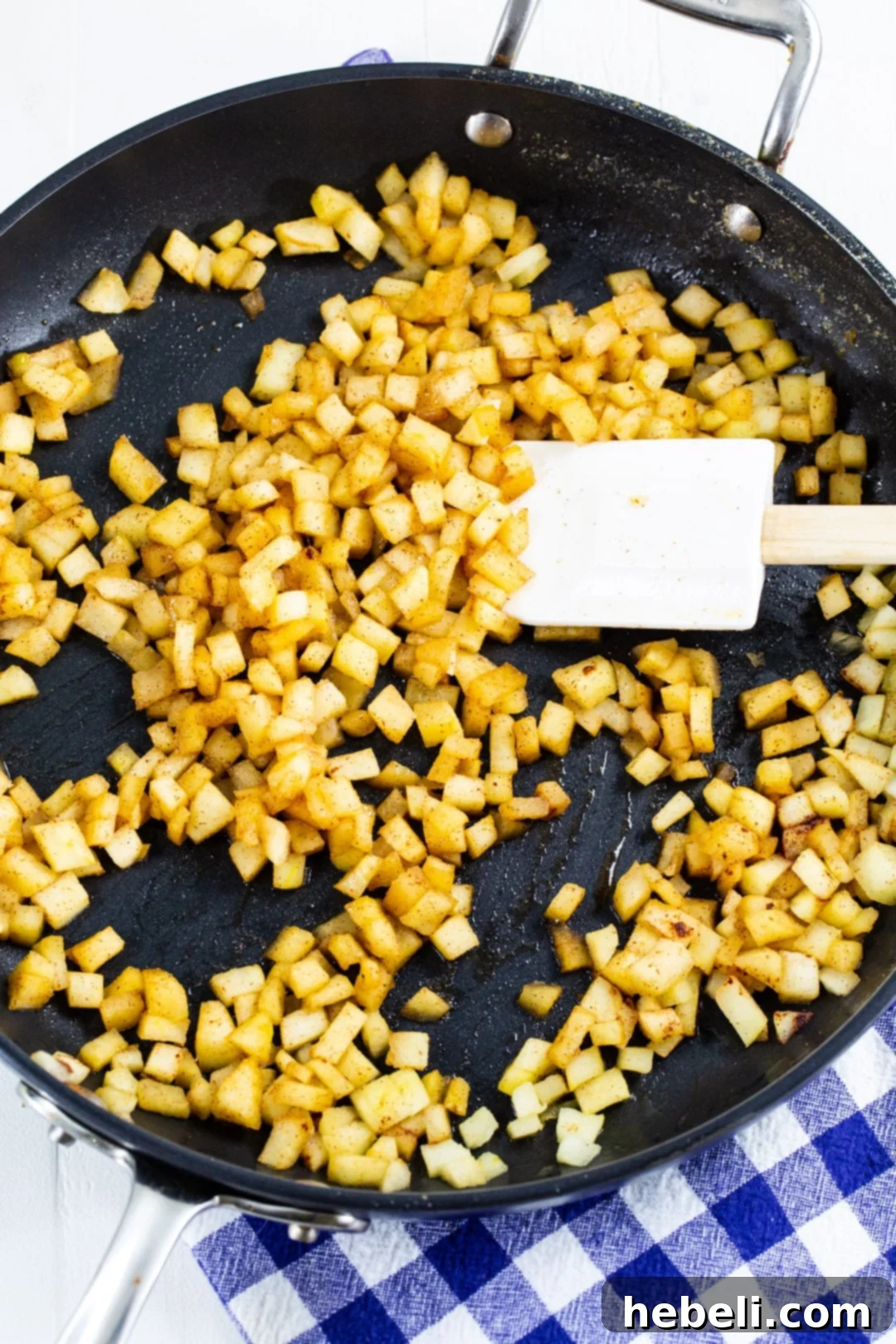 Finely diced apples cooking in a skillet with butter and spices.