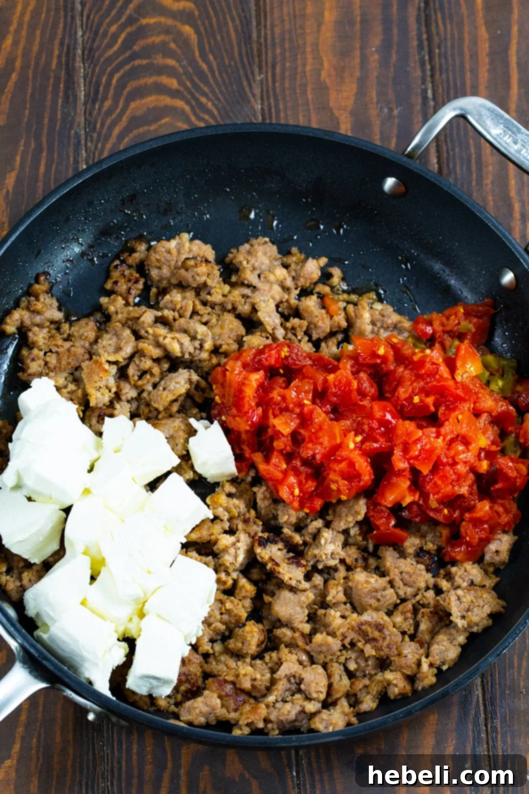 Three key ingredients for Rotel Sausage Dip – sausage, cream cheese cubes, and a can of Rotel – laid out in a skillet before cooking.