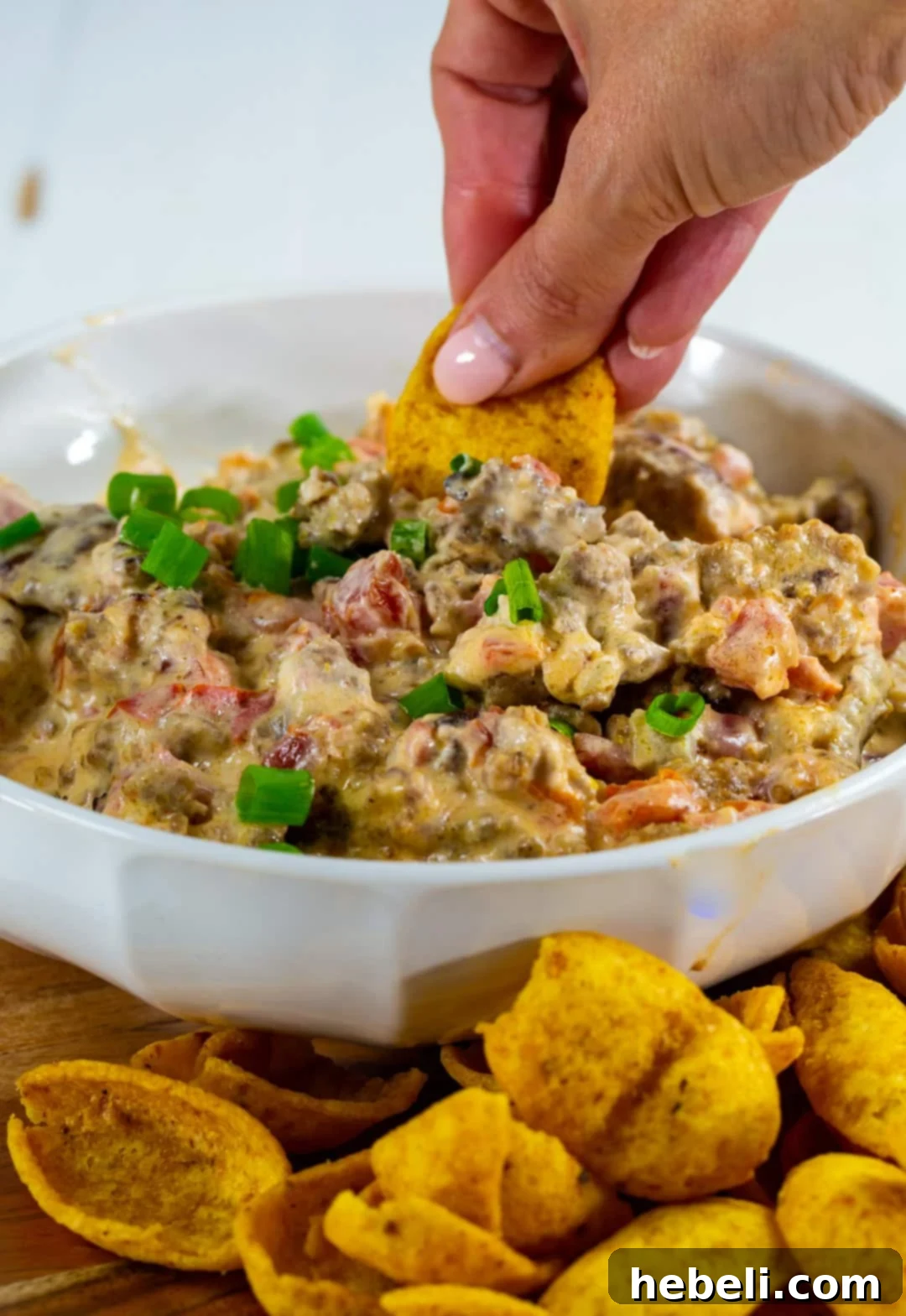 A hand reaching in with a Frito chip to scoop up the warm, cheesy 3-Ingredient Rotel Sausage Dip, emphasizing its irresistible appeal.