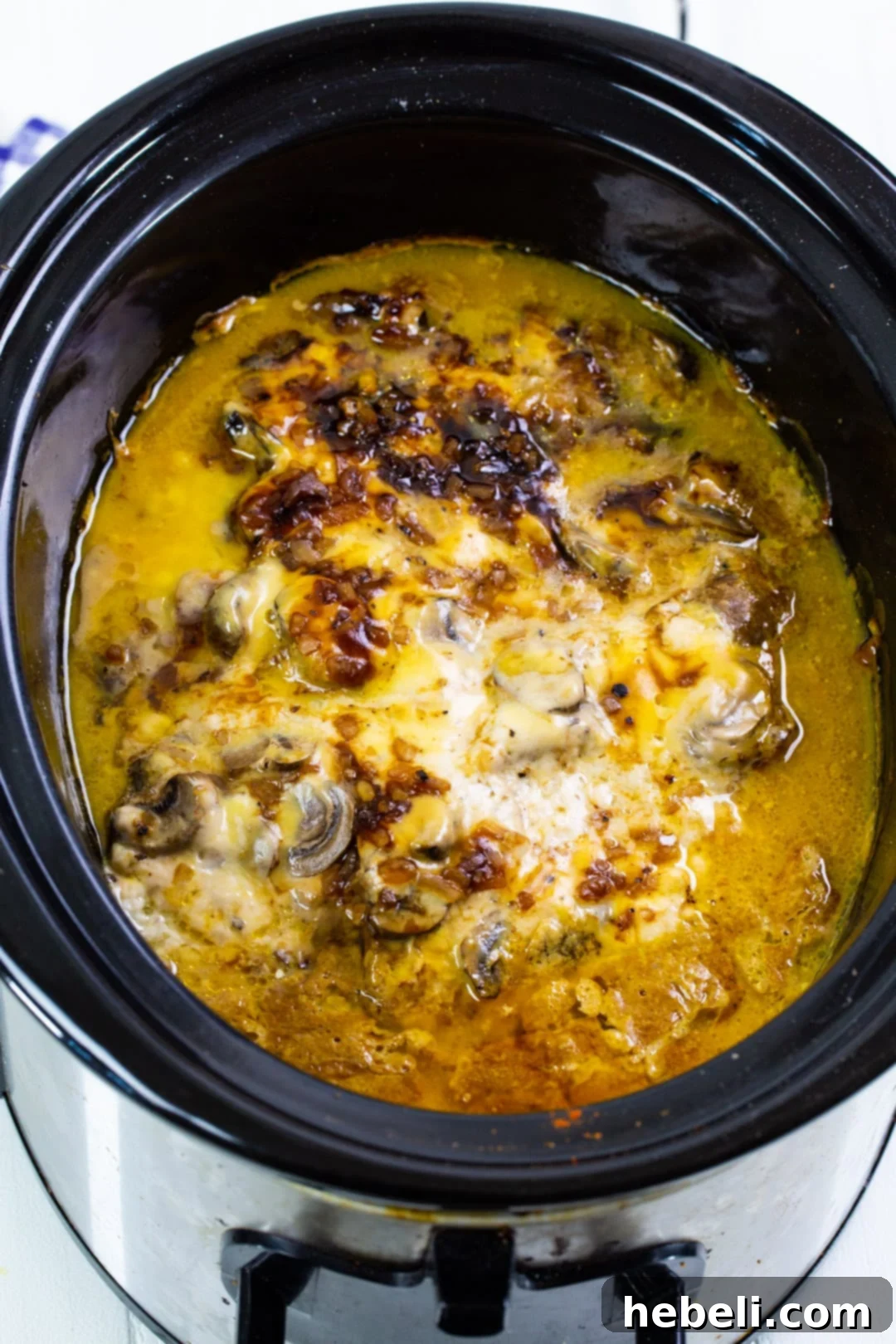 Pork chops cooking in the slow cooker, submerged in a rich, creamy sauce with mushrooms and onions.