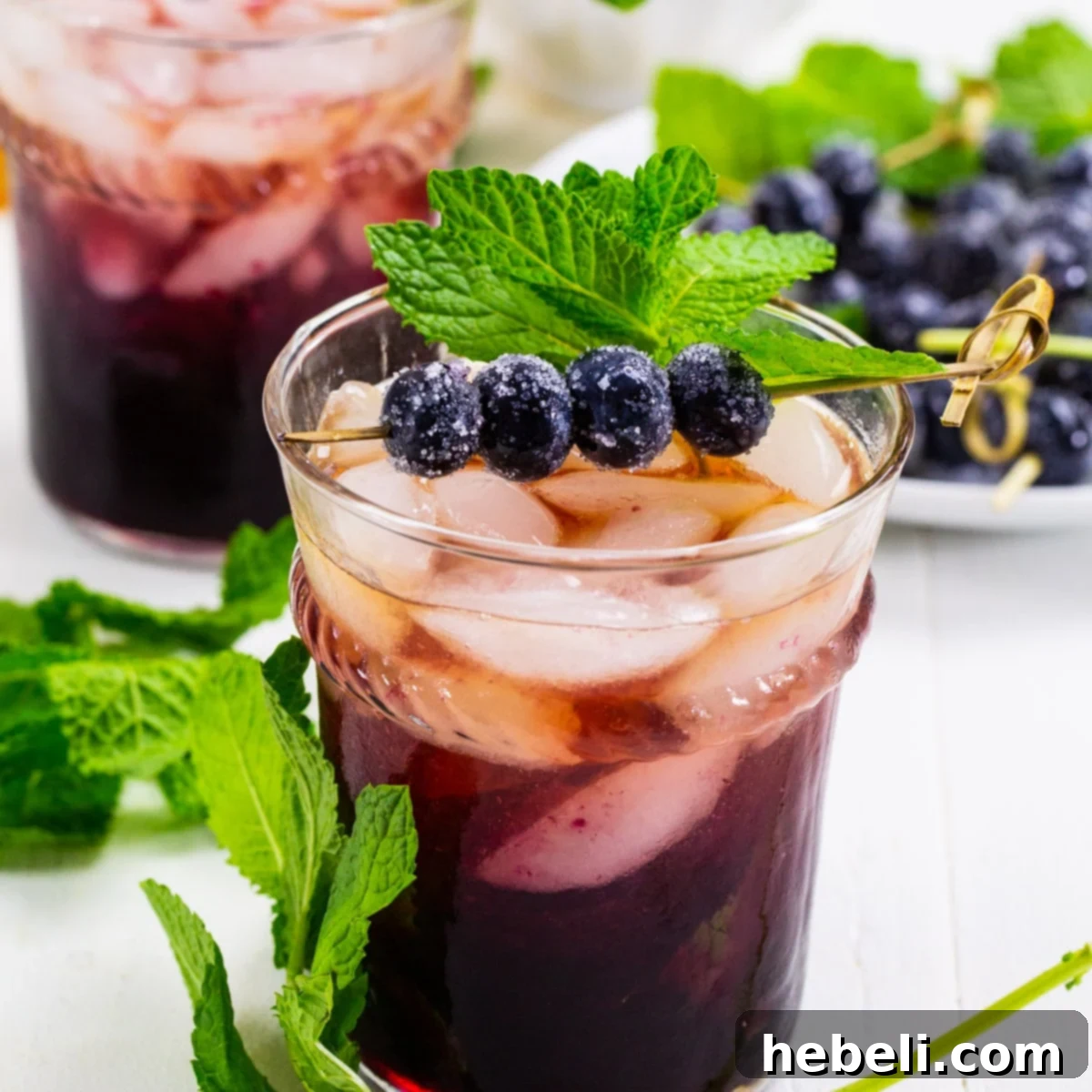 A vibrant Blueberry Mint Julep, garnished with fresh mint sprigs and glistening sugared blueberries, served in a classic julep cup filled with crushed ice.