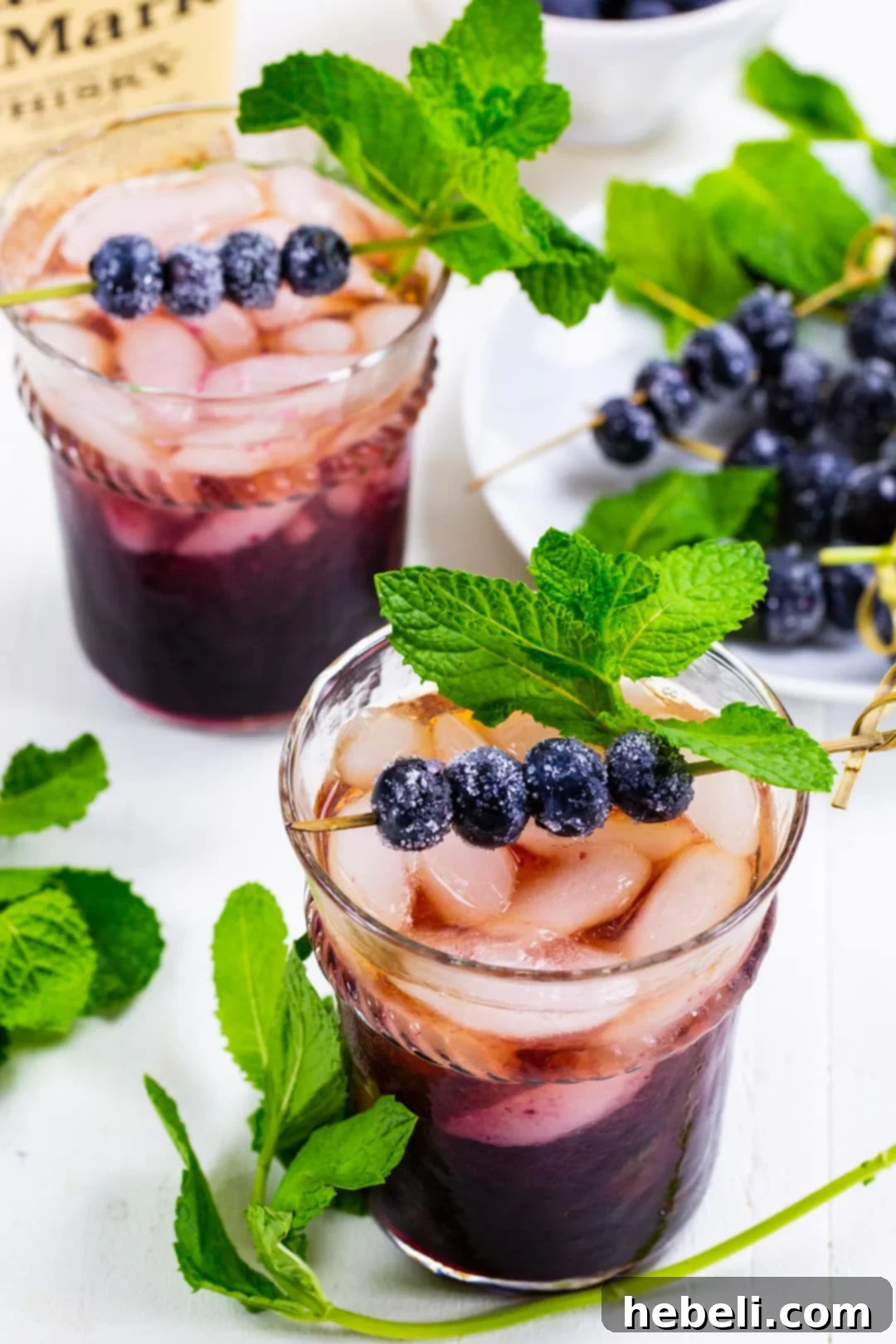 Two elegantly prepared Blueberry Mint Juleps, showcasing their rich color and inviting garnishes, ready to be enjoyed.