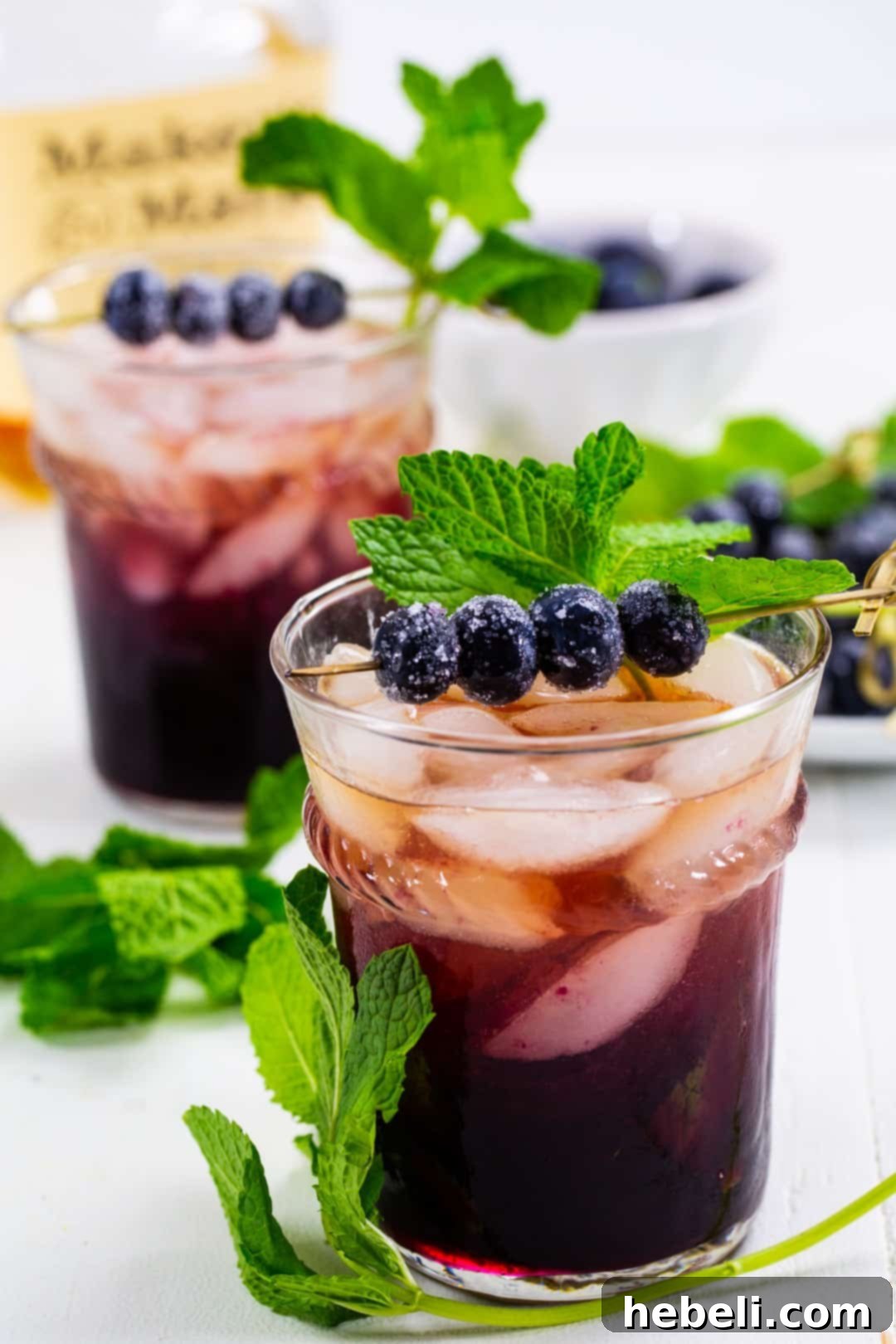 A refreshing Mint Julep adorned with a generous sprig of fresh mint and a scattering of sugared blueberries, served in a julep cup.