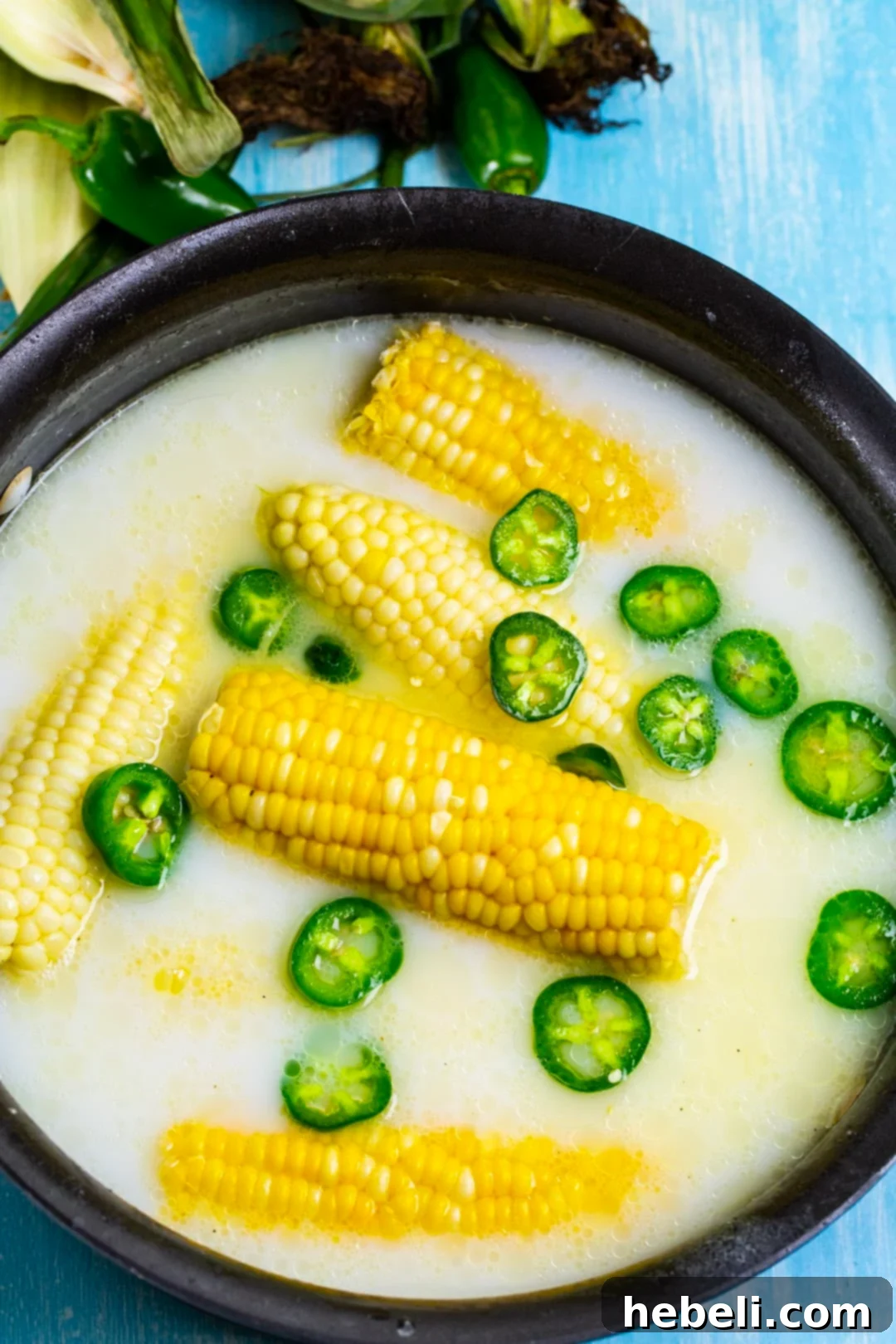 Sweet Heat Honey Butter Corn 3 Close-up of corn on the cob and sliced jalapenos simmering in a creamy milk bath in a pot.