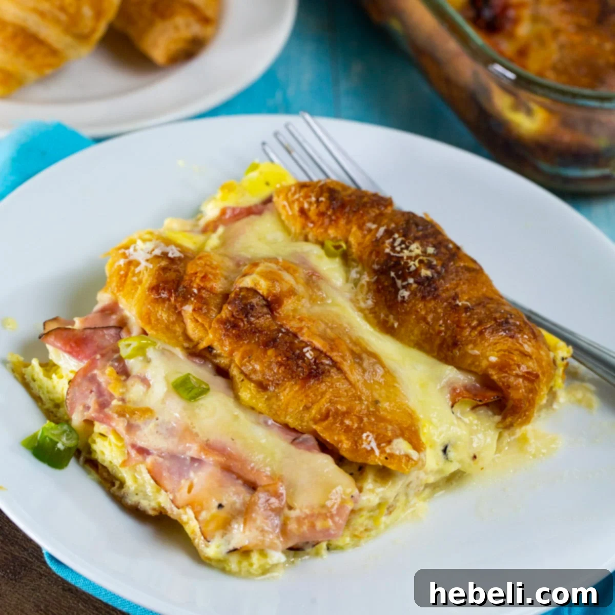 Savory Ham and Cheese Croissant Bake 2 A delectable slice of Stuffed Ham and Cheese Croissant Casserole, golden brown and perfectly baked, resting on a small plate, ready to be enjoyed.