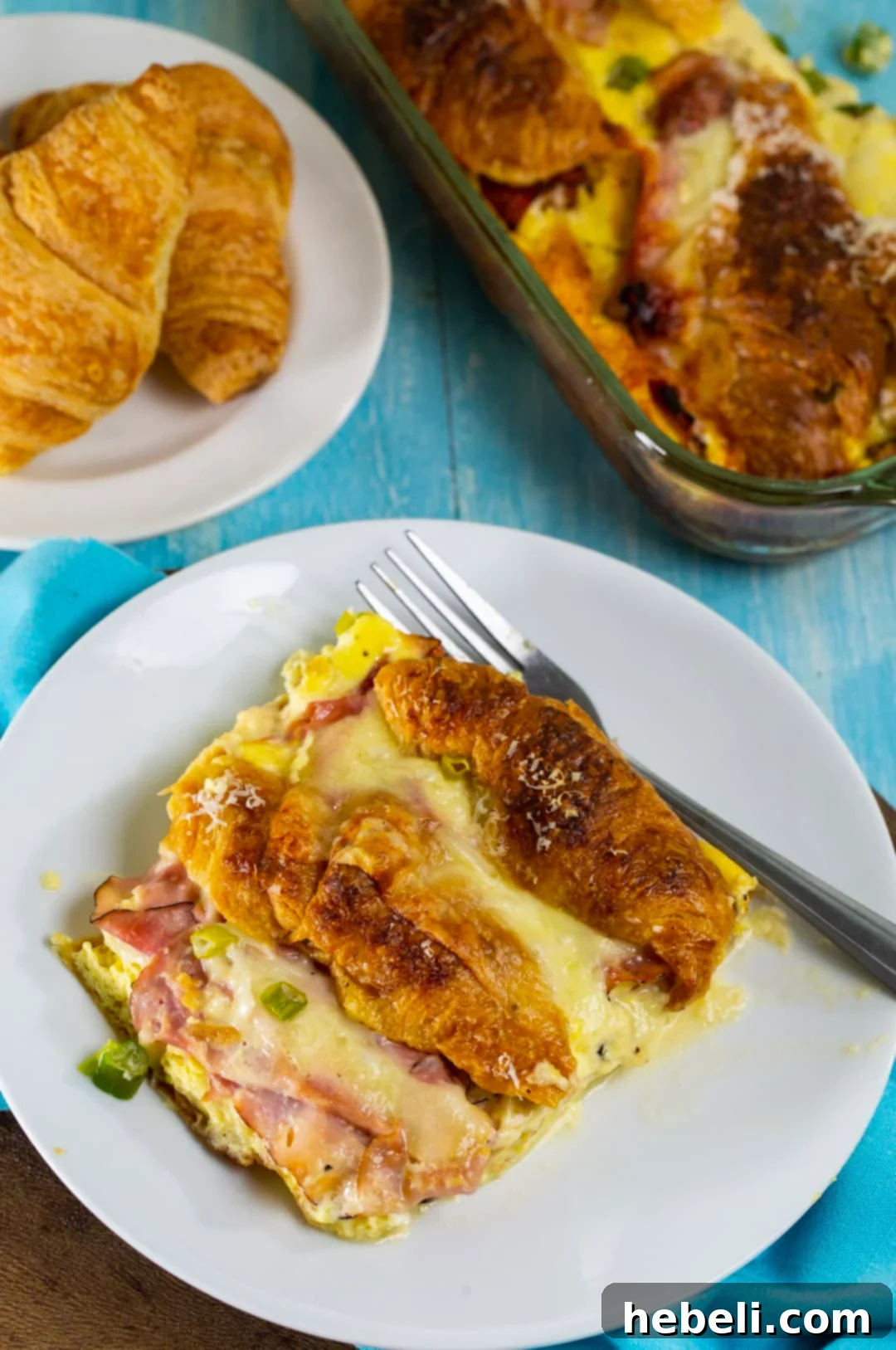 Savory Ham and Cheese Croissant Bake 6 A serving of the casserole on a white plate, with a basket of fresh croissants in the background, highlighting the golden-brown exterior and gooey interior.