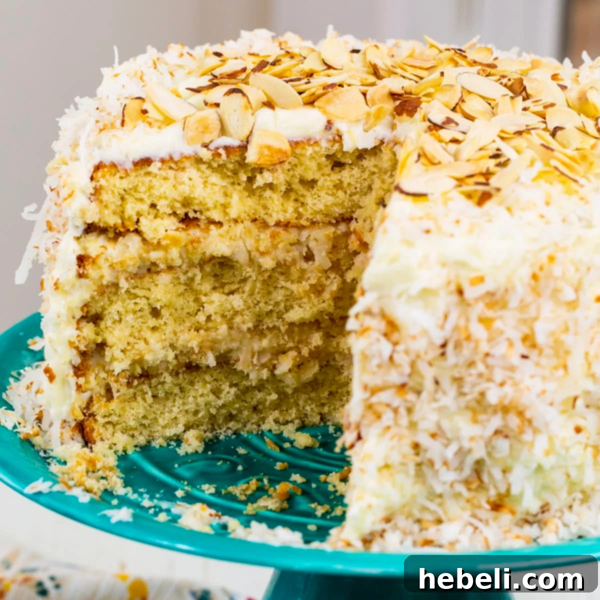 A beautifully frosted Coconut Almond Cream Cake with a slice cut out, revealing its moist layers and creamy filling.