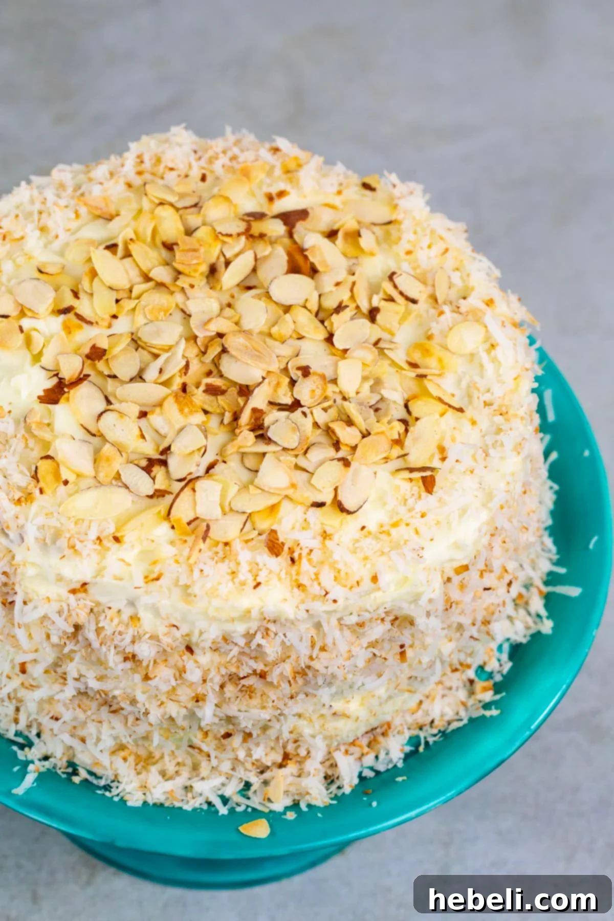 A grand, frosted Coconut Almond Cream Cake adorned with toasted almond slices, presented on a decorative cake stand.