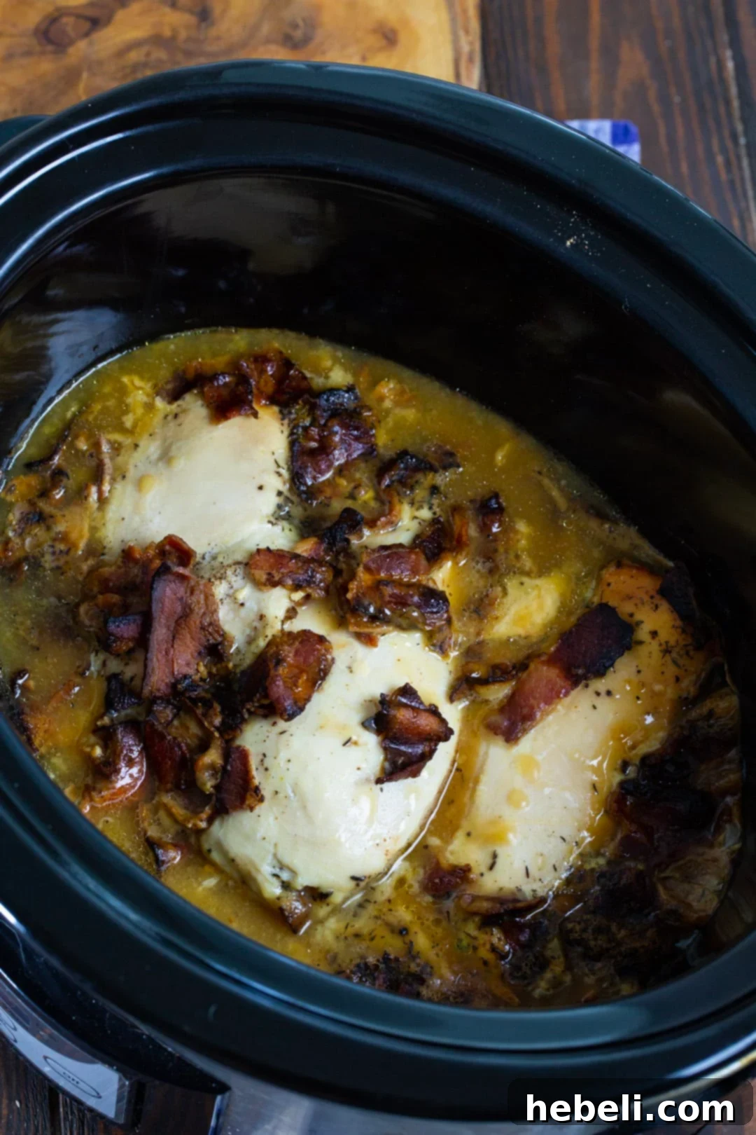 The cooked slow cooker chicken, glistening in its rich, creamy bacon gravy, ready to be removed and served.