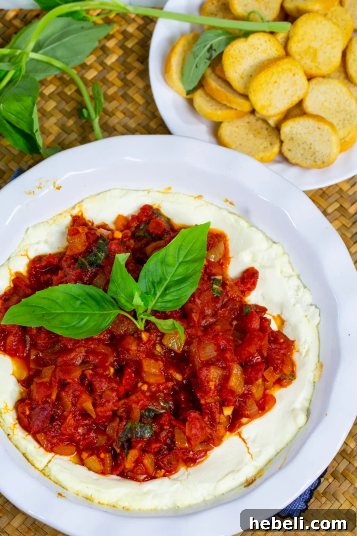 Baked Goat Cheese Dip served in a pie plate alongside toasted baguette slices on a wooden board.