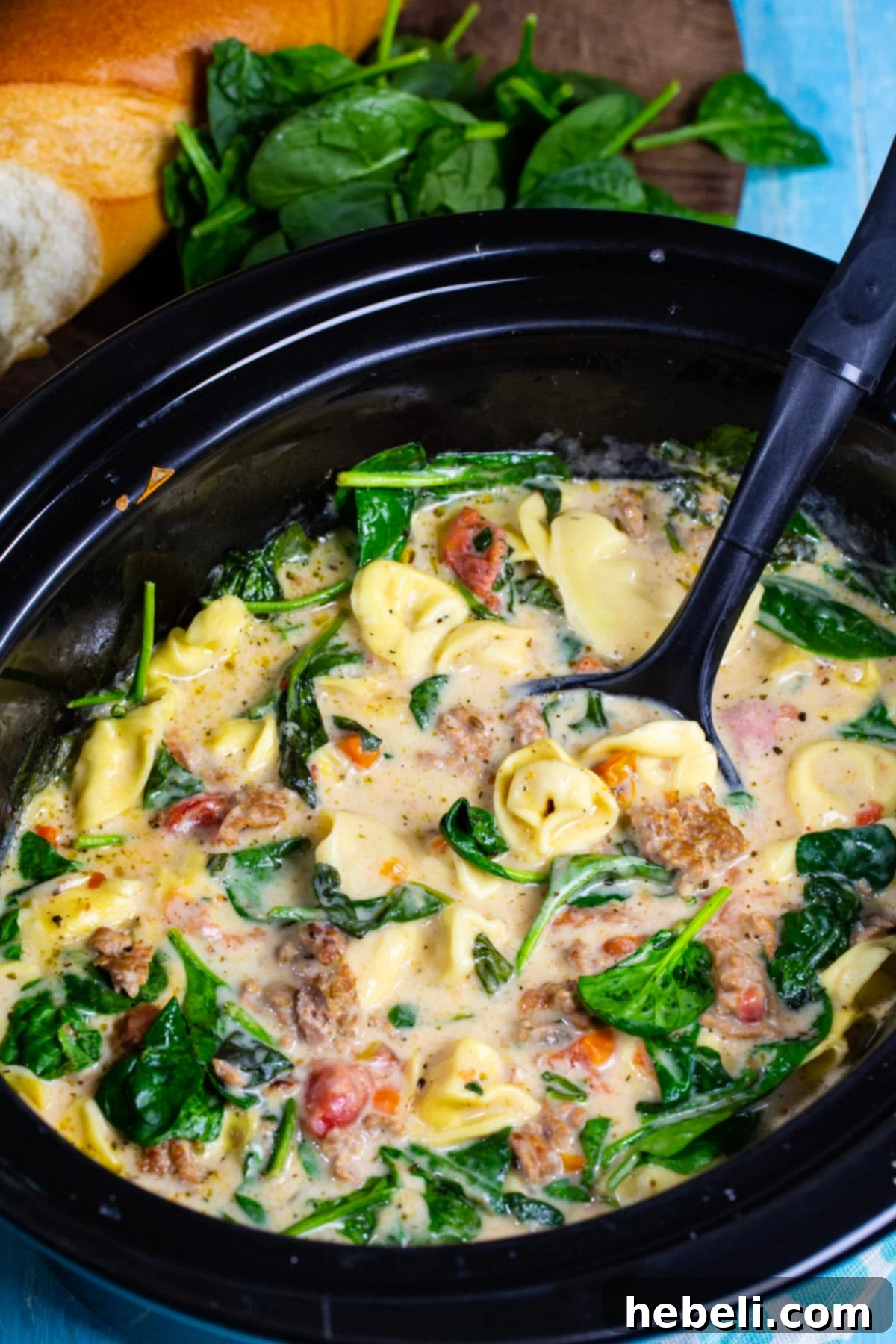 A ladle expertly scooping a generous portion of steaming Slow Cooker Creamy Tortellini and Sausage Soup from a slow cooker pot, highlighting its rich texture and steam.