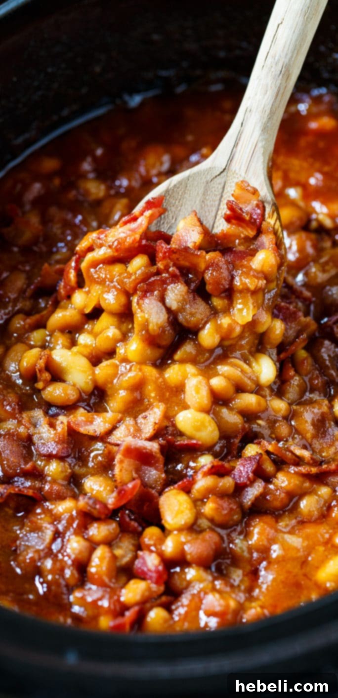A wooden spoon scooping up Slow Cooker Bourbon Baked Beans from a crockpot, showcasing the thick, rich sauce.