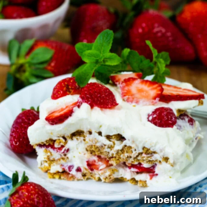 A delectable piece of Strawberry Icebox Dessert on a small white plate, showcasing its creamy layers and fresh strawberry garnish.