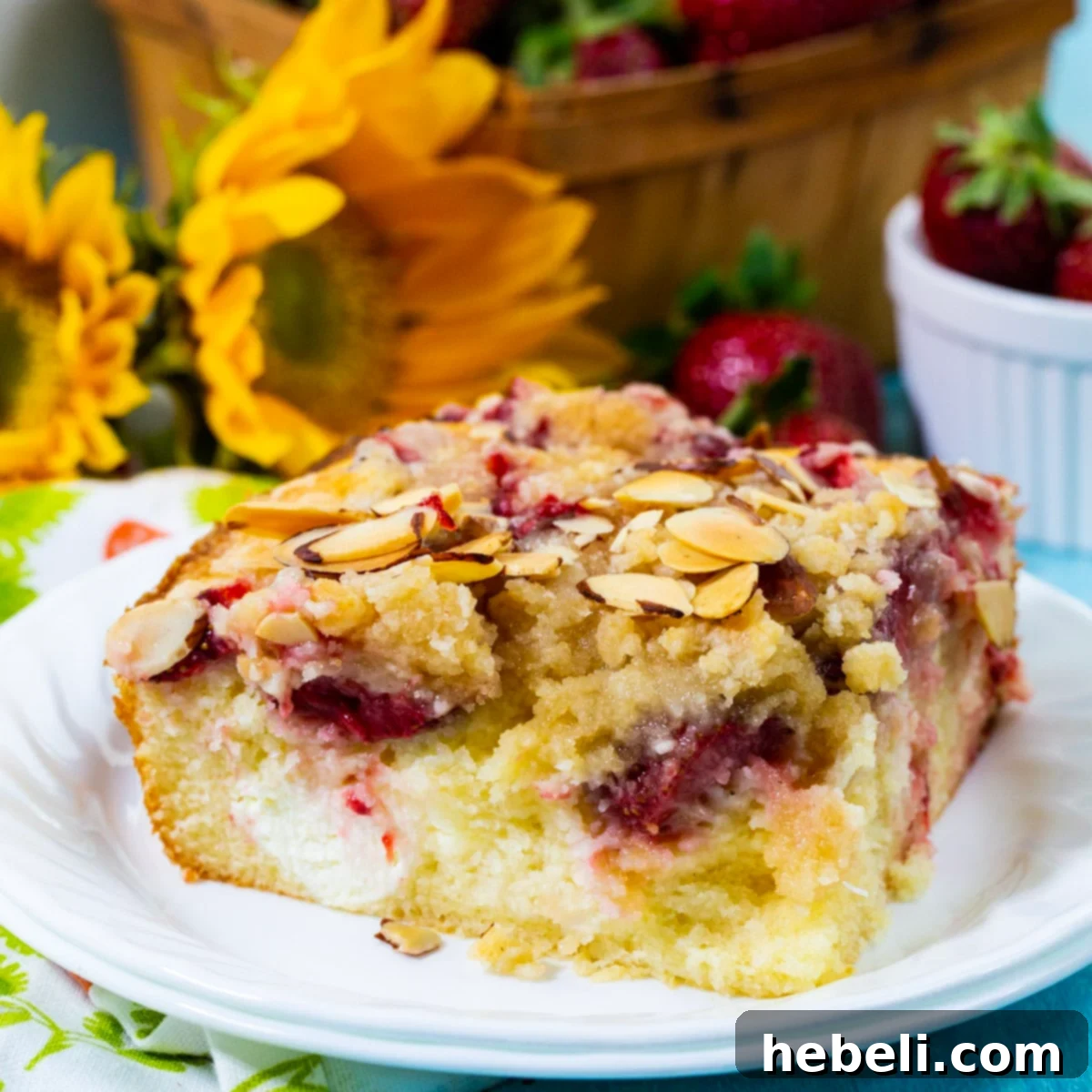 A beautifully presented slice of Strawberry Cream Cheese Coffee Cake on a pristine white plate, showcasing the layers of moist cake, vibrant red strawberries, creamy white cheese swirls, and golden brown streusel topping.