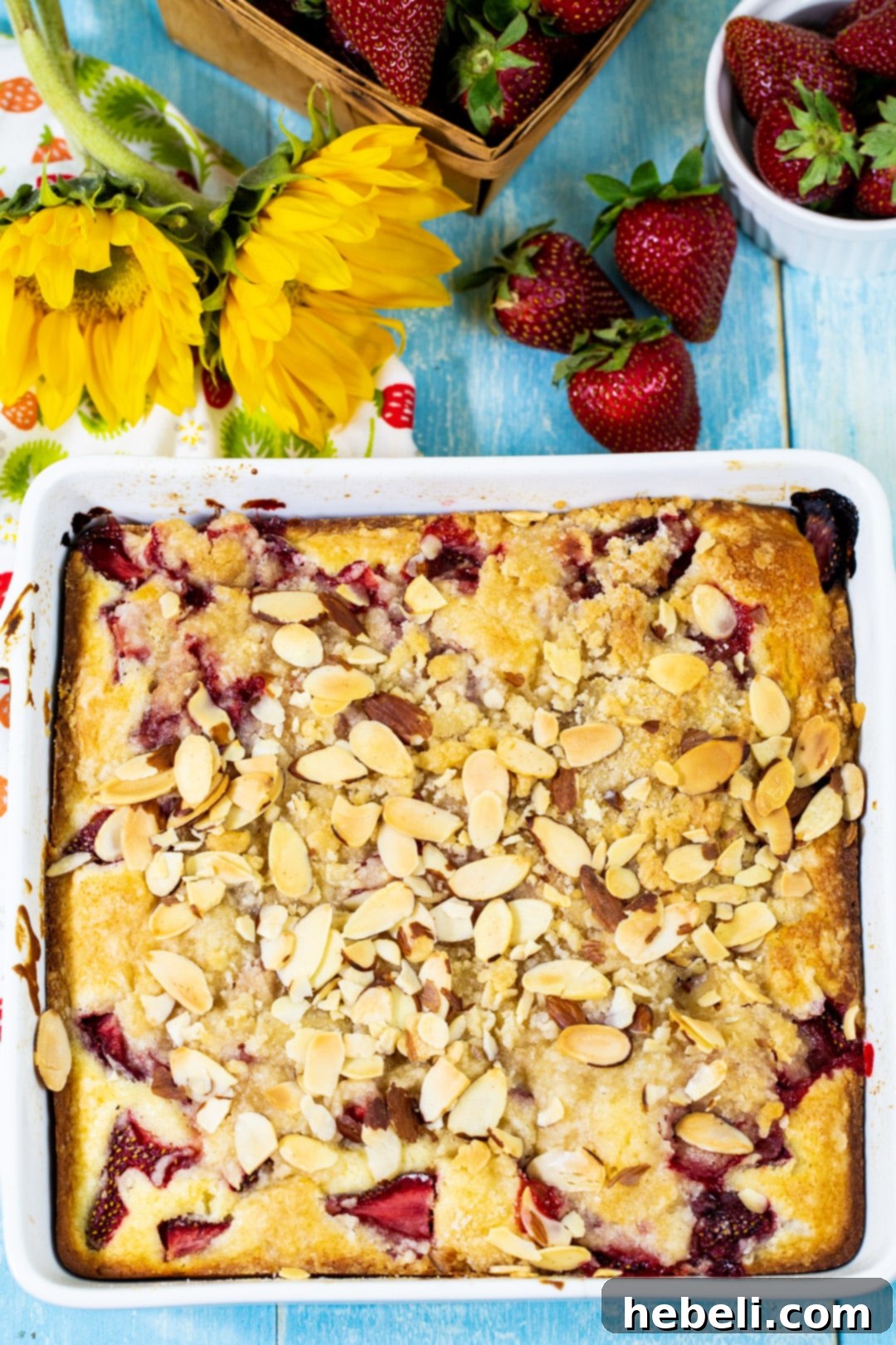 Strawberry Cream Cheese Coffee Cake baking in a clear glass dish, showing the bubbly fruit and golden crumb topping before the final almond sprinkle.