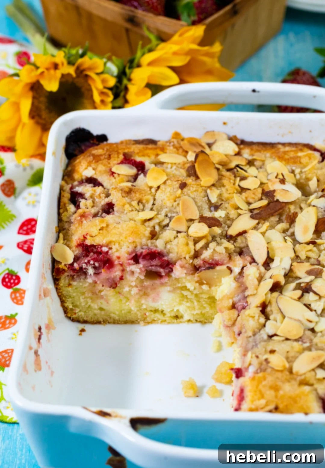 A whole Strawberry Cream Cheese Coffee Cake in its baking dish with one square slice already removed, showcasing the moist, fruit-laden interior and perfect crumbly topping.