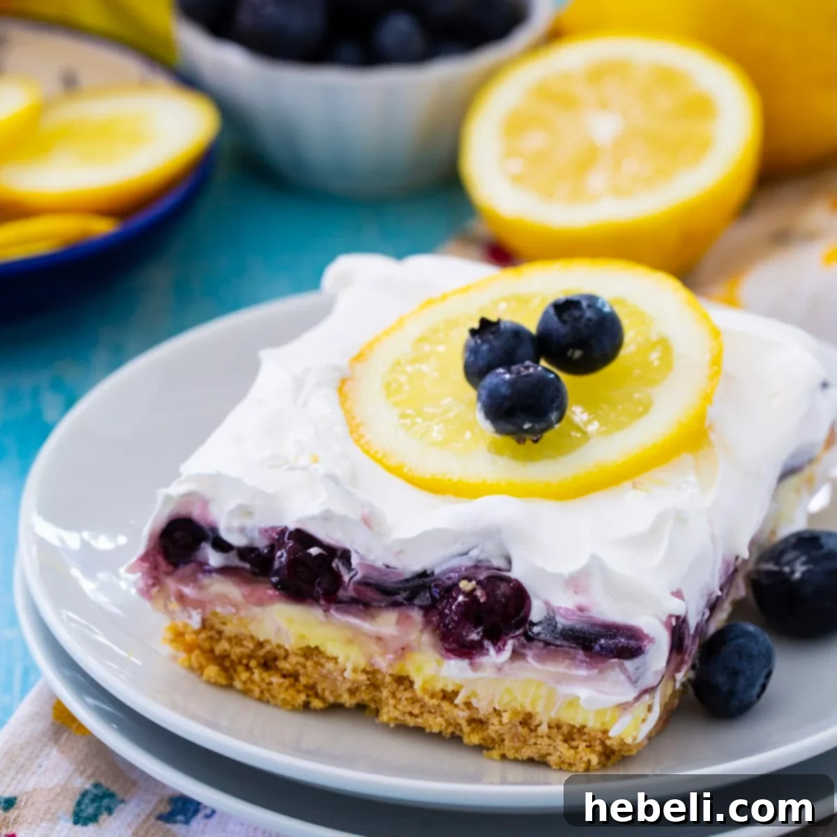 A beautiful slice of Blueberry Lemon Layer Dessert, showcasing its distinct layers of graham cracker crust, creamy lemon, and fruity blueberry, served on a white plate with a fork, ready to be enjoyed.