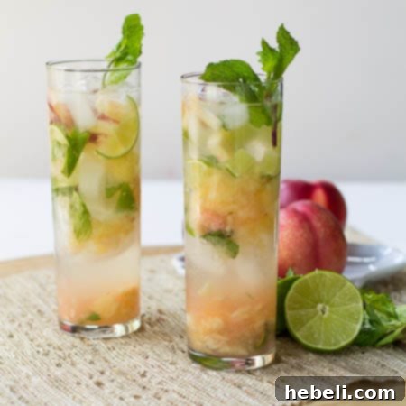 Summer Nectarine Mojito 3 A close-up shot of Nectarine Mojitos served in tall glasses, accompanied by fresh lime halves and sliced nectarines on a rustic surface.