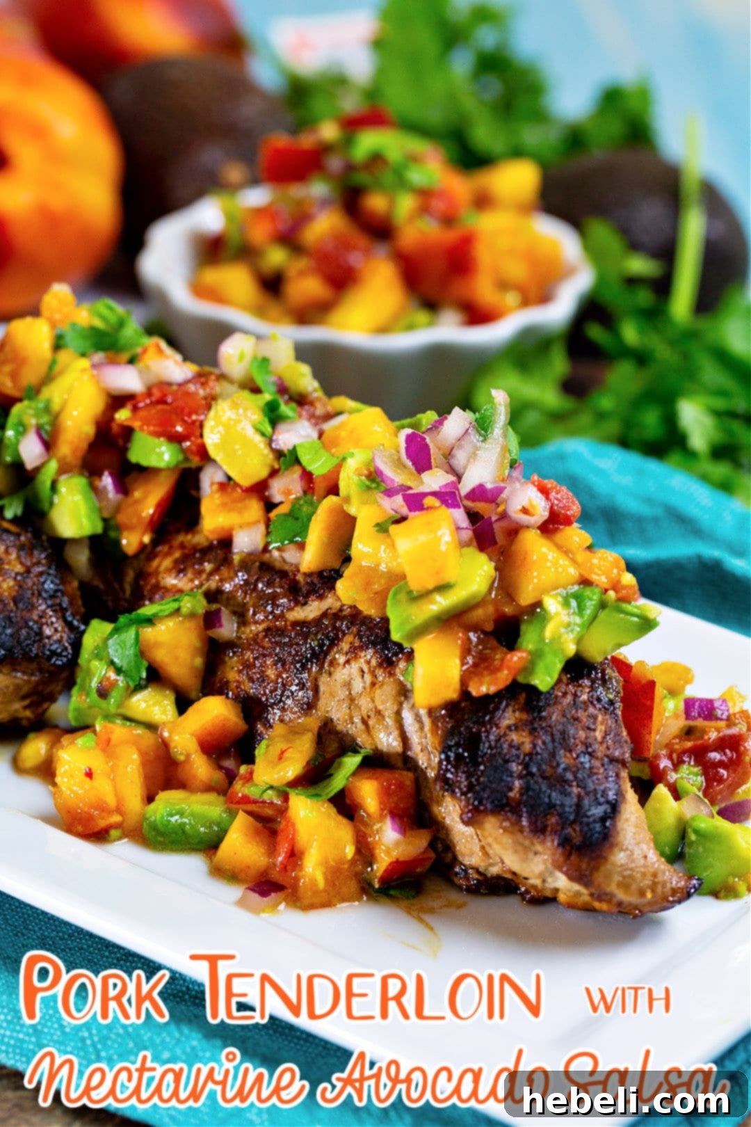 Seared Pork Tenderloin with Bright Nectarine Avocado Salsa 5 Full view of a whole cooked pork tenderloin generously covered with a colorful, fresh fruit salsa on a dark serving platter.