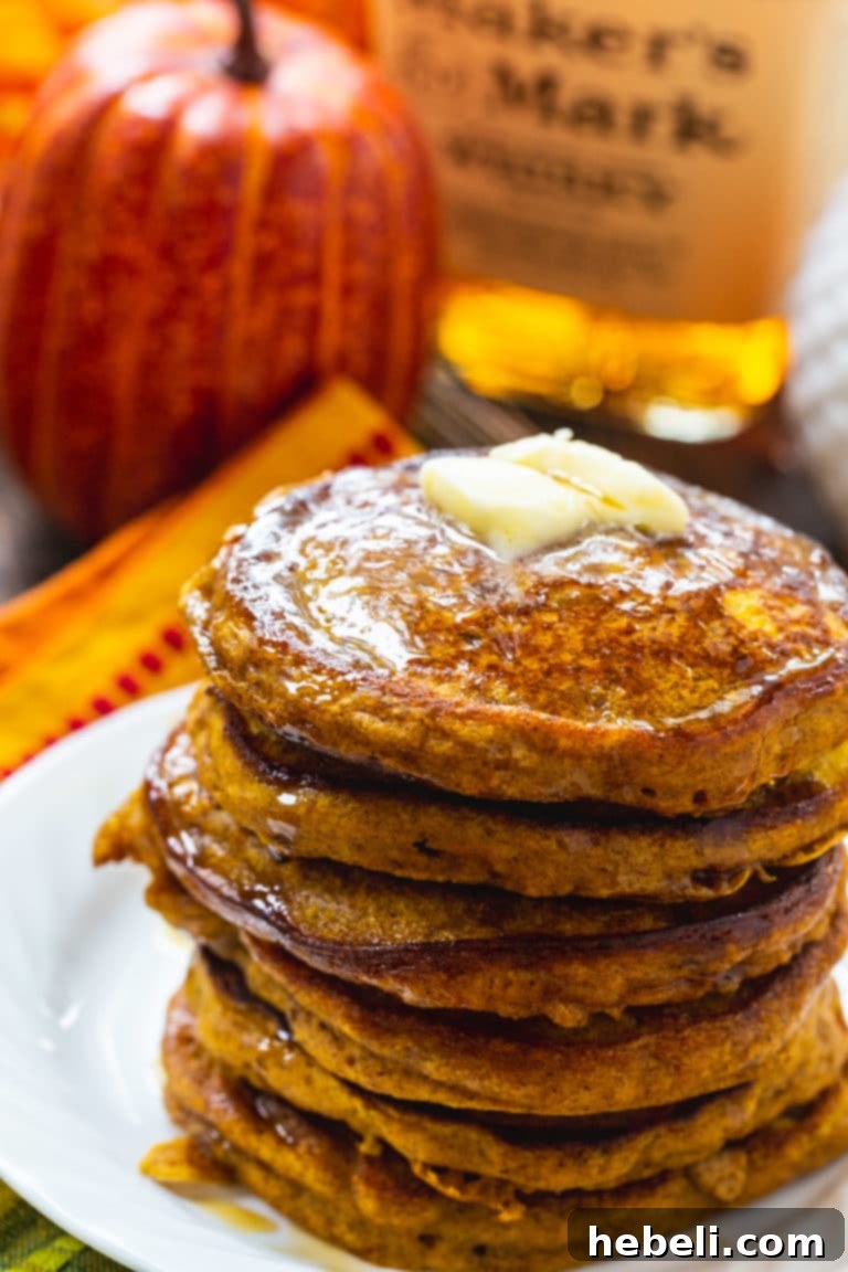 Maple Kissed Bourbon Vanilla Pumpkin Pancakes 3 A beautifully styled stack of pumpkin pancakes, garnished with whipped cream and a light dusting of cinnamon, against a rustic fall backdrop.
