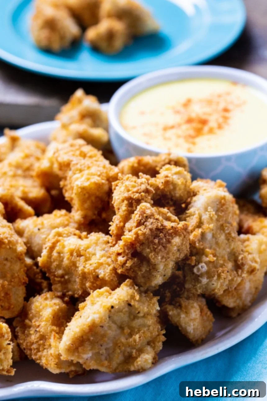 Crispy Chicken Nuggets piled high on a white plate with a side bowl of honey mustard dipping sauce.