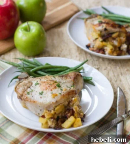 Pork Chops Stuffed with Apple and Bacon on a white plate with green beans. Apples in background.