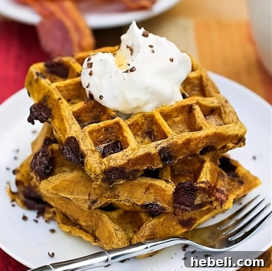 Golden Pumpkin Waffles generously topped with fluffy whipped cream and a drizzle of maple syrup, perfect for a cozy fall morning.