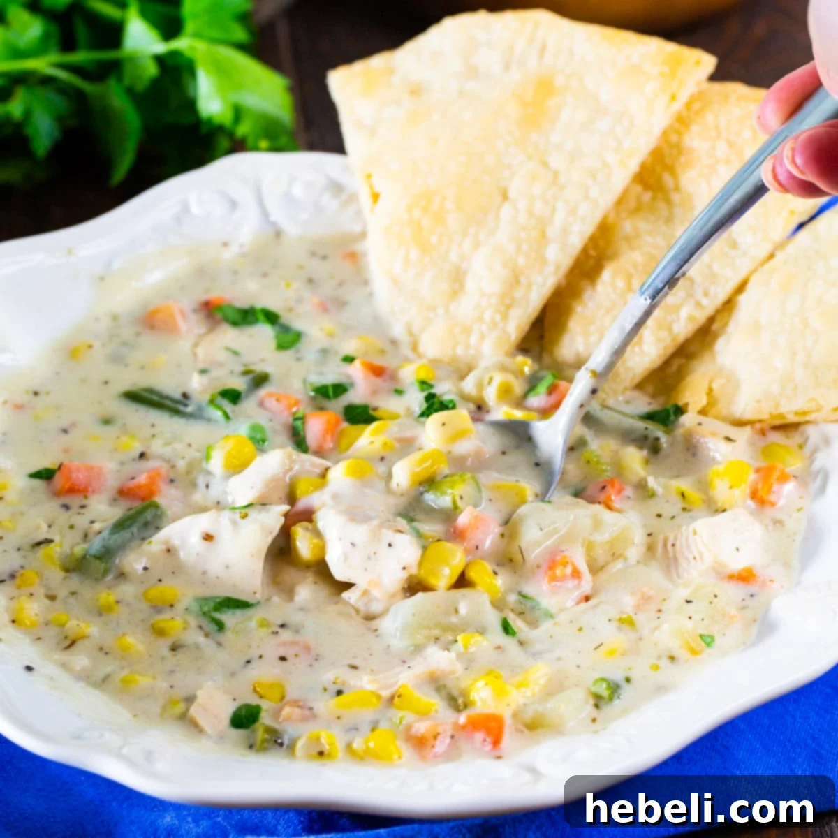 Hearty Chicken Pot Pie Soup 2 Spoon scooping up creamy chicken pot pie soup out of a rustic ceramic bowl, highlighting tender chicken, potatoes, and vibrant green vegetables.