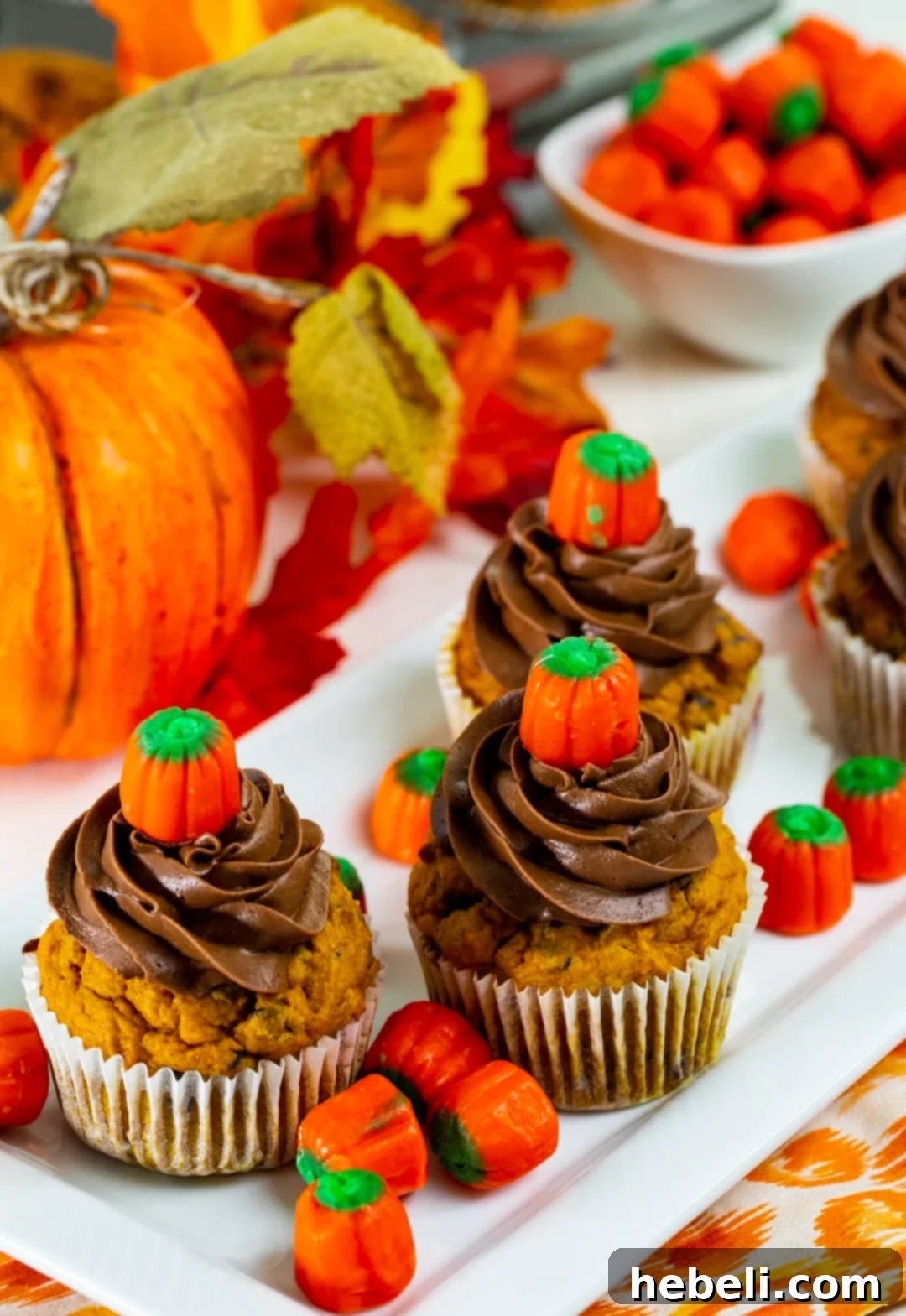Freshly baked Pumpkin Chocolate Chip Cupcakes, artfully arranged and surrounded by charming candy corn pumpkins, highlighting their inviting appeal.