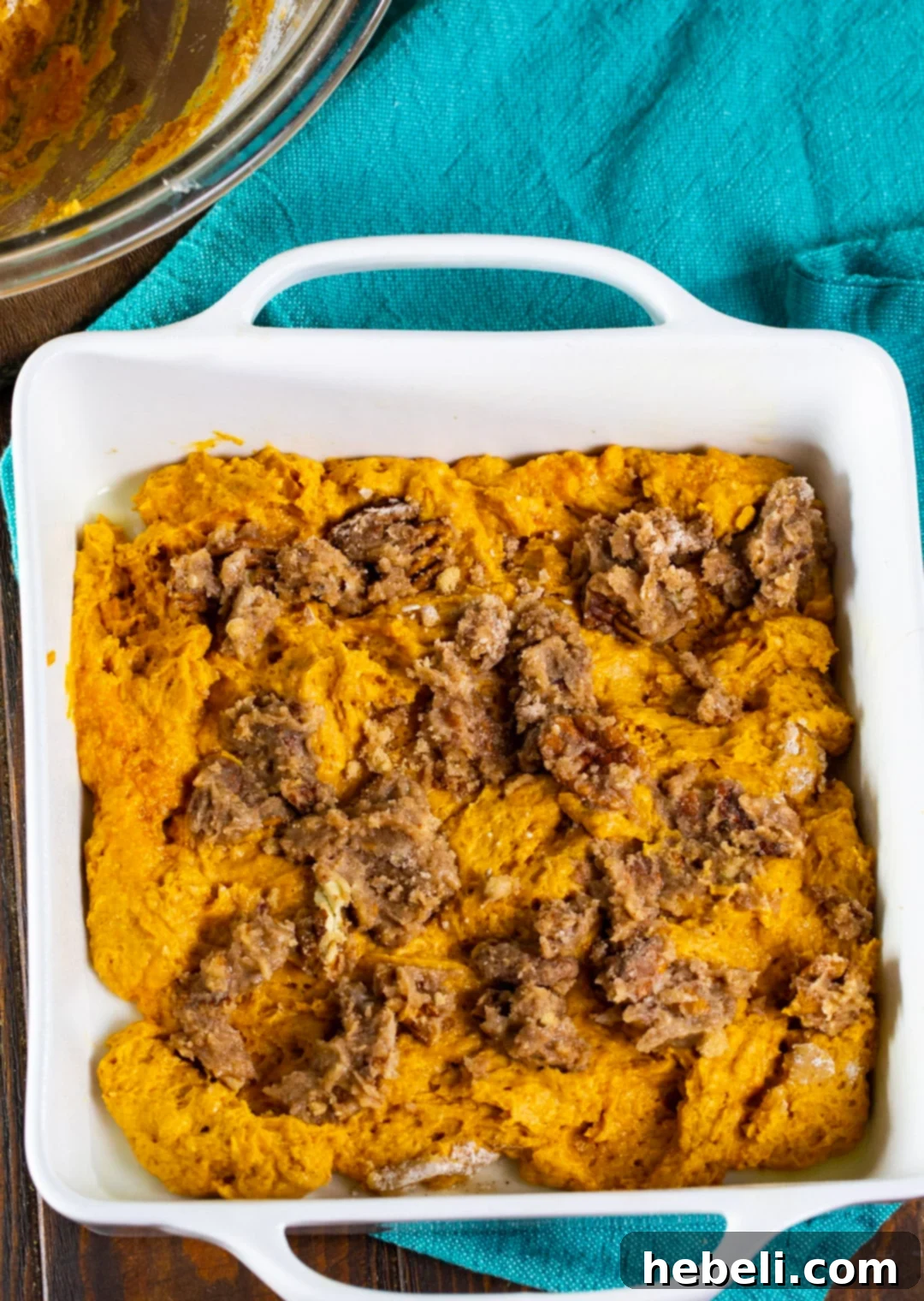 Streusel topping evenly spread over unbaked pumpkin coffee cake batter in a baking dish.