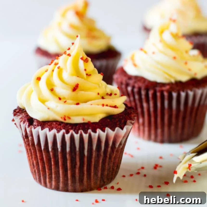 Close-up of vibrant Red Velvet Cupcakes with a generous swirl of cream cheese frosting, garnished with festive red sprinkles.