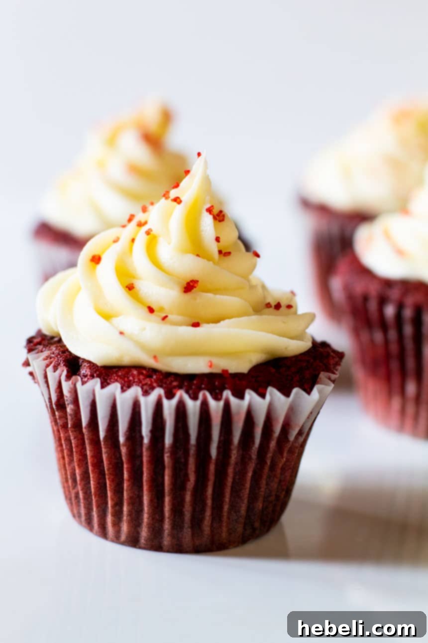 A single Red Velvet Cupcake, perfectly frosted with cream cheese, sitting on a white surface, ready to be enjoyed.