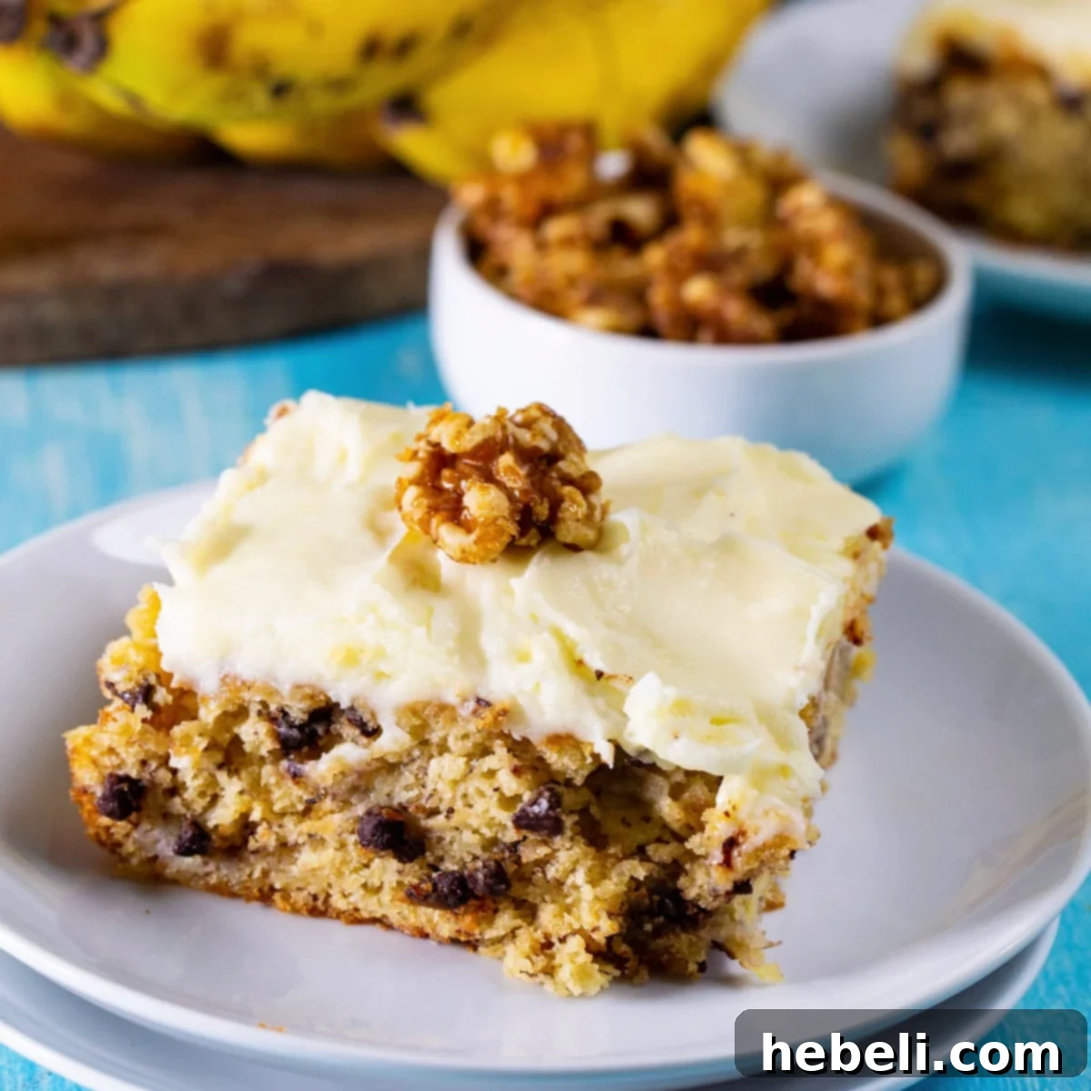 A slice of Banana Cake with Cream Cheese Frosting and candied walnuts on a small white plate, ready to be enjoyed.