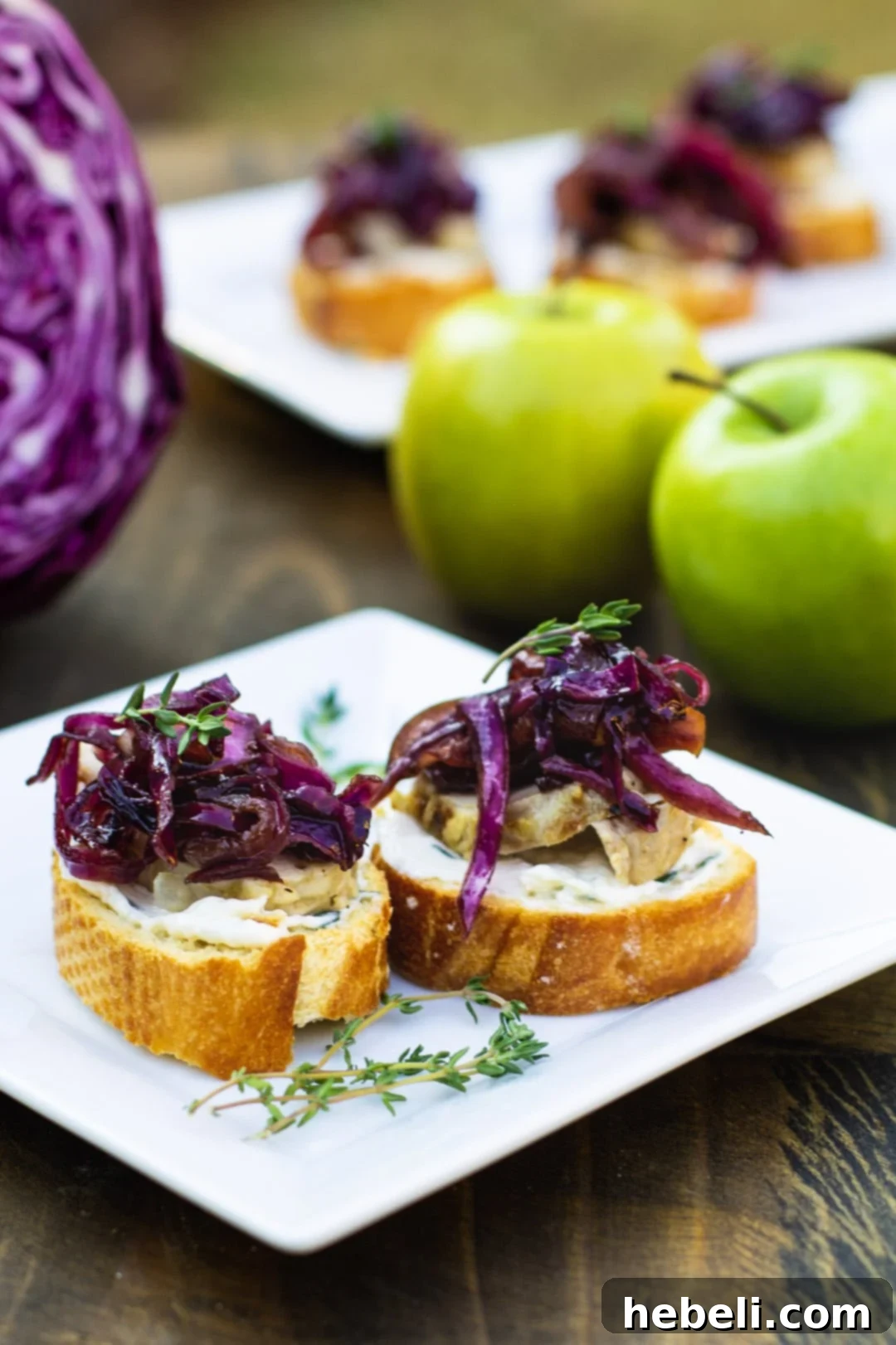 Pork Crostini arranged on a platter, with a bowl of sweet and sour red cabbage and apples in the background.