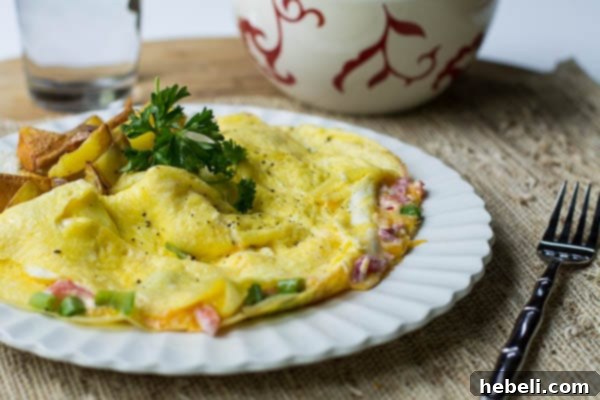 Fluffy pimiento cheese omelet served on a white plate with a side of golden home fries, ready to be enjoyed.