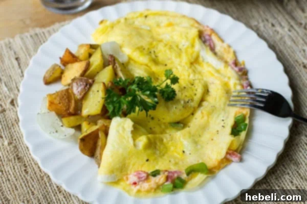 Close-up of a pimiento cheese omelet, revealing its creamy, melted filling and served with crispy home fries and a fork, highlighting its rich texture.