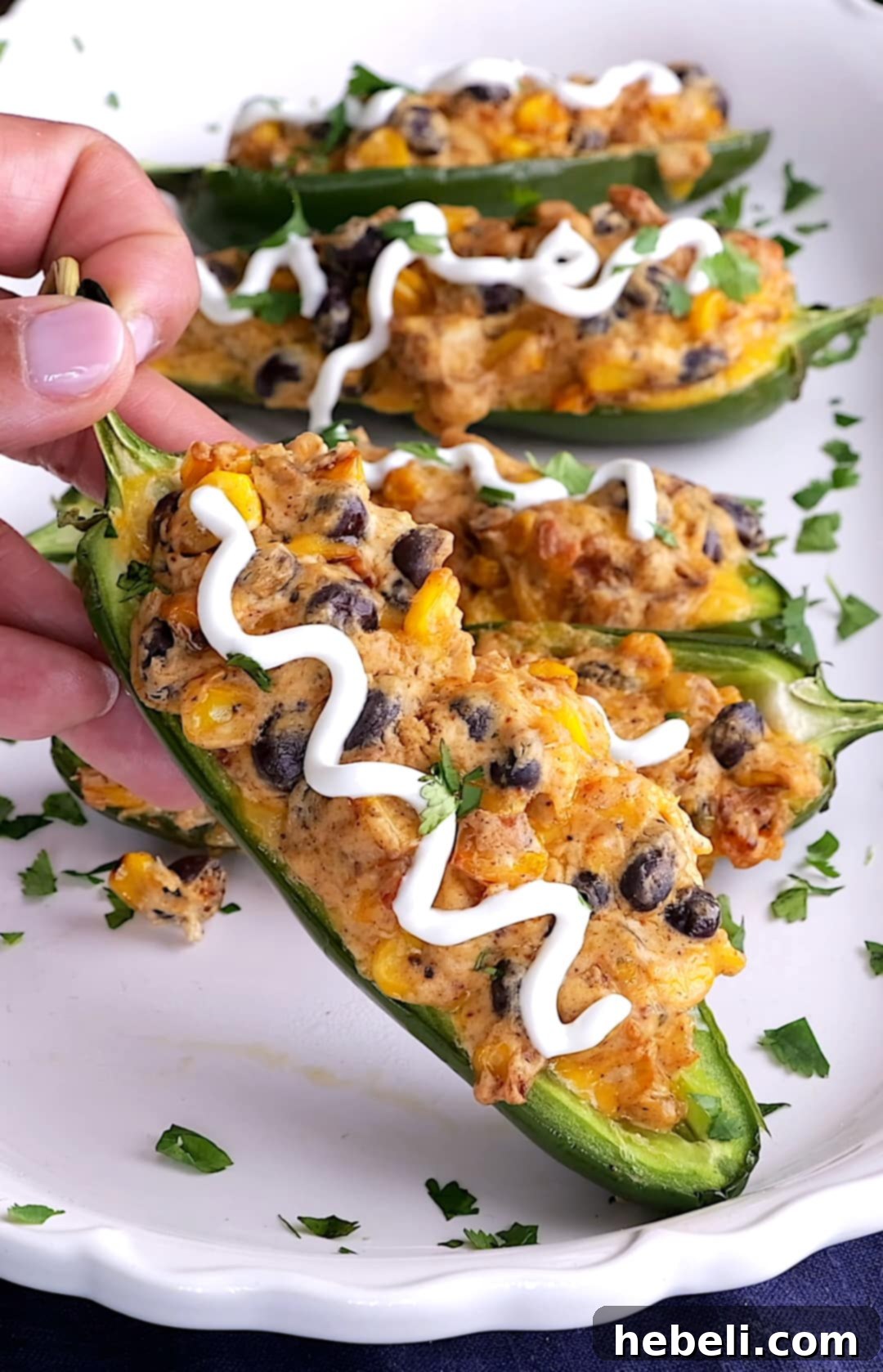 Fiesta Black Bean and Corn Jalapenos 5 Hand reaching for a perfectly baked Black Bean and Corn Stuffed Jalapeno