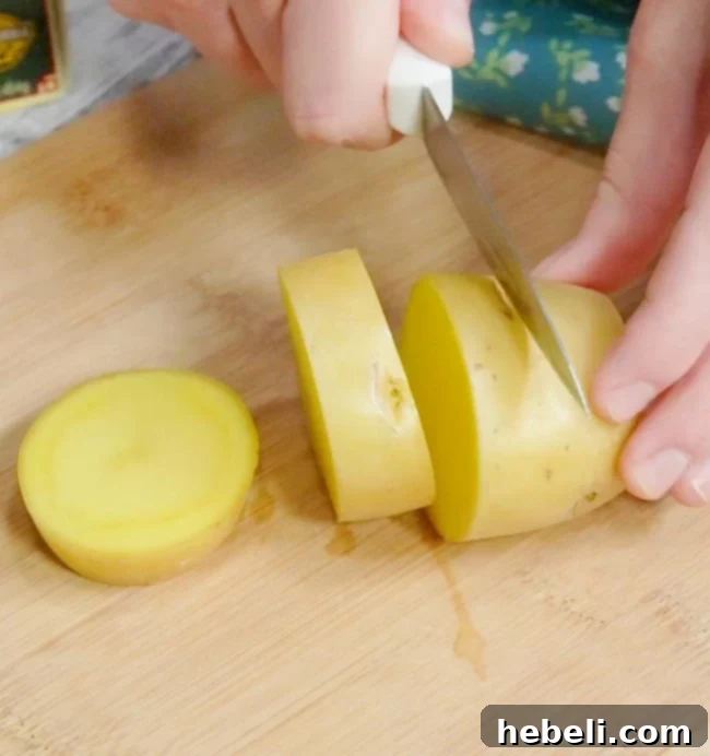 A chef's knife expertly slicing a potato into uniform, thick disks, preparing them for the Melting Potatoes recipe.