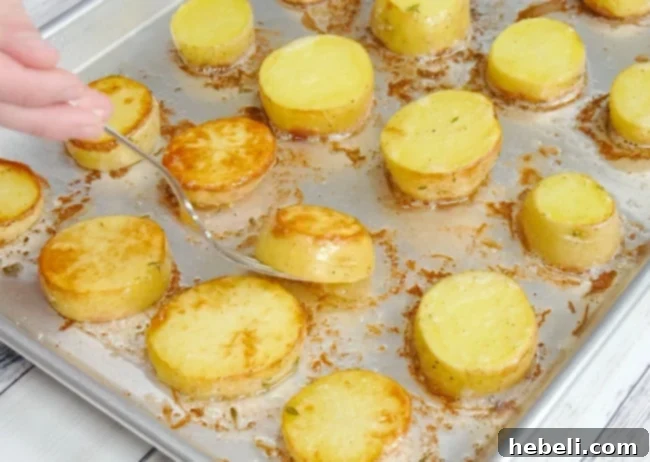 A spatula gently turning potato slices on a baking sheet, revealing their golden-brown undersides after the initial roasting period.