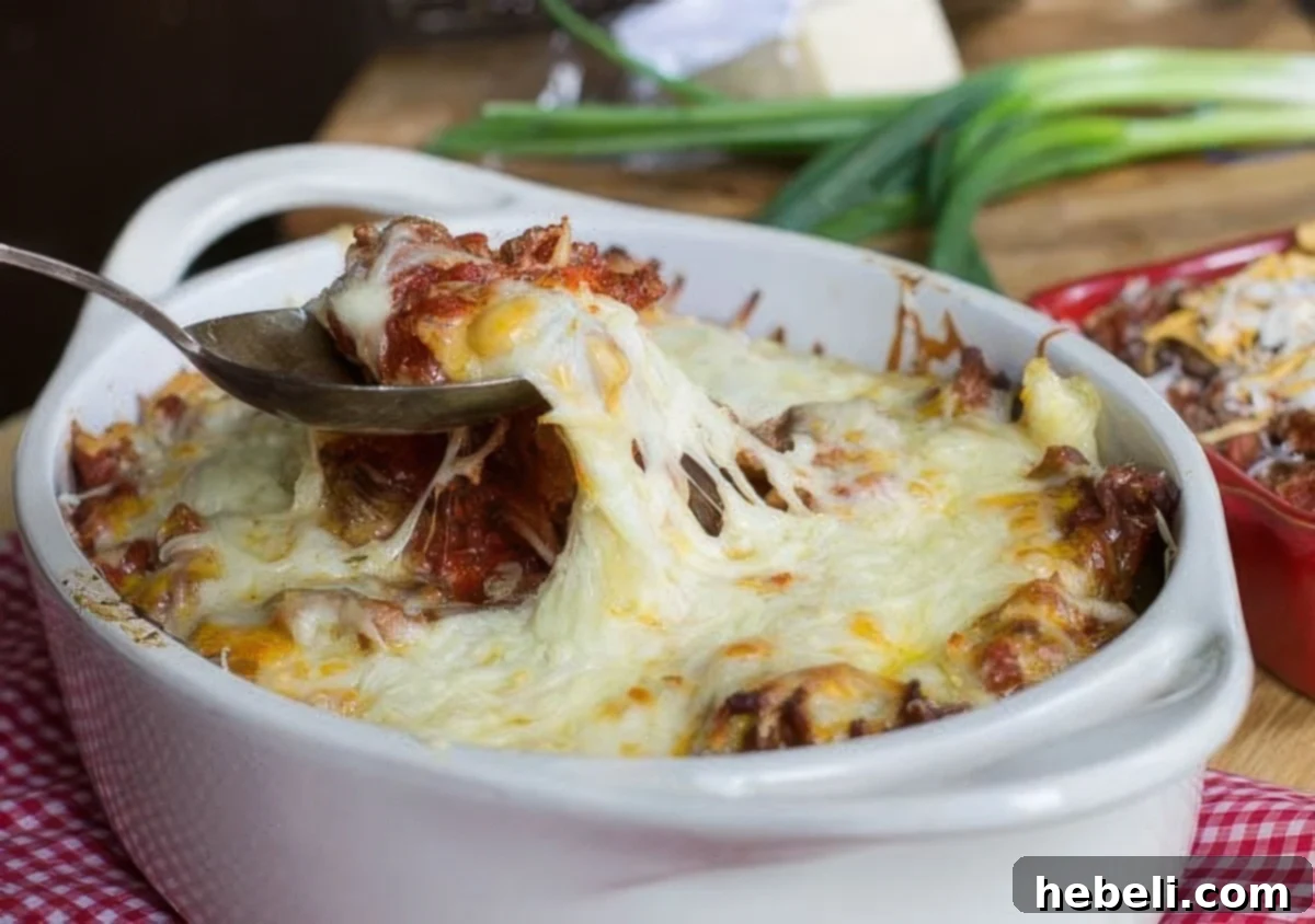 Comforting Ground Beef Supper 2 A spoon scooping up a generous portion of cheesy Homestyle Ground Beef Casserole from a baking dish.