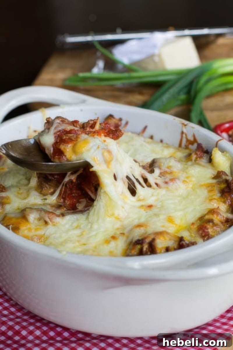 Comforting Ground Beef Supper 3 Close-up of a spoon scooping a portion of Homestyle Ground Beef Casserole from a white baking dish, showcasing the creamy noodles and rich beef sauce.